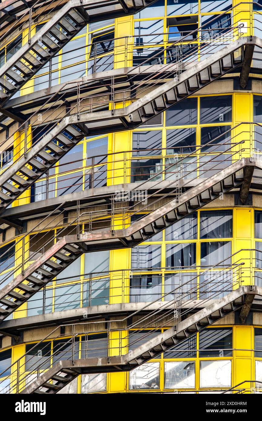 Un antico edificio industriale caratterizzato da prominenti scale di emergenza e grandi finestre gialle, che mostrano il suo design architettonico storico. Foto Stock