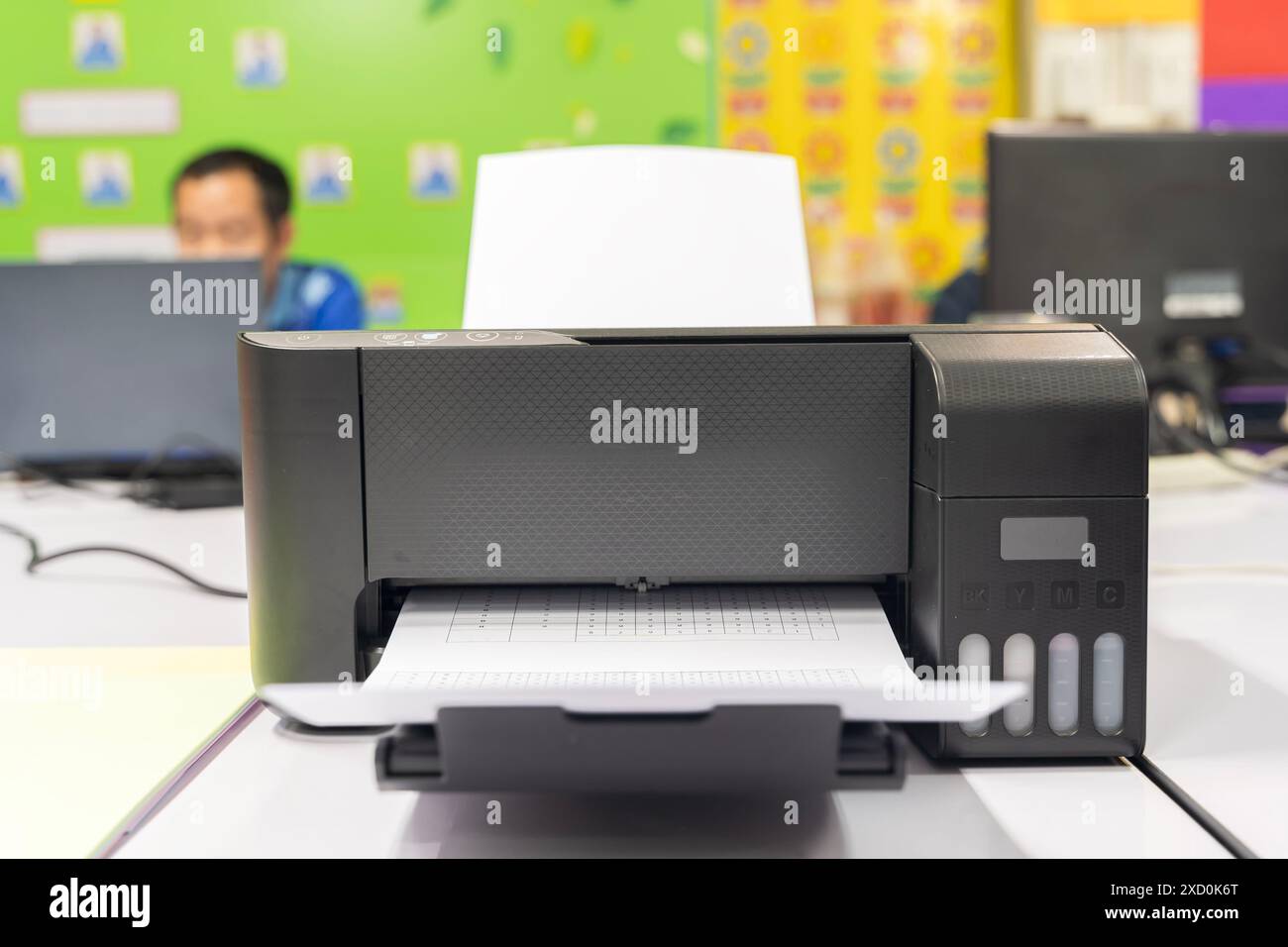 Una stampante nera è aperta e contiene un foglio di carta bianco all'interno. La stampante si trova su una scrivania di fronte a un computer Foto Stock