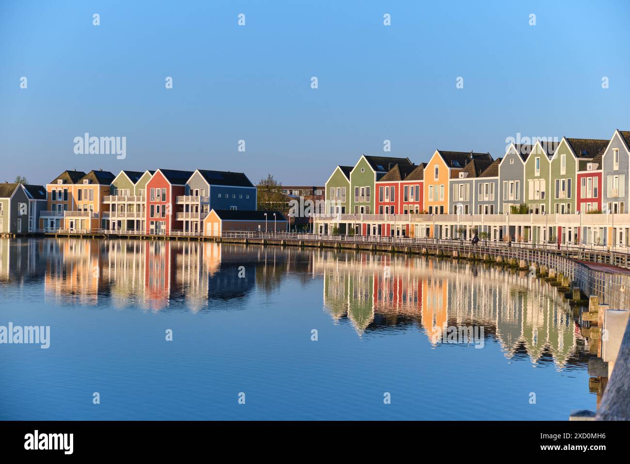 Houten, Paesi Bassi - 23 aprile 2024. Colorate case in legno sul lago si riflettono nell'acqua del lago De Rietplas contro un cielo azzurro. Foto Stock