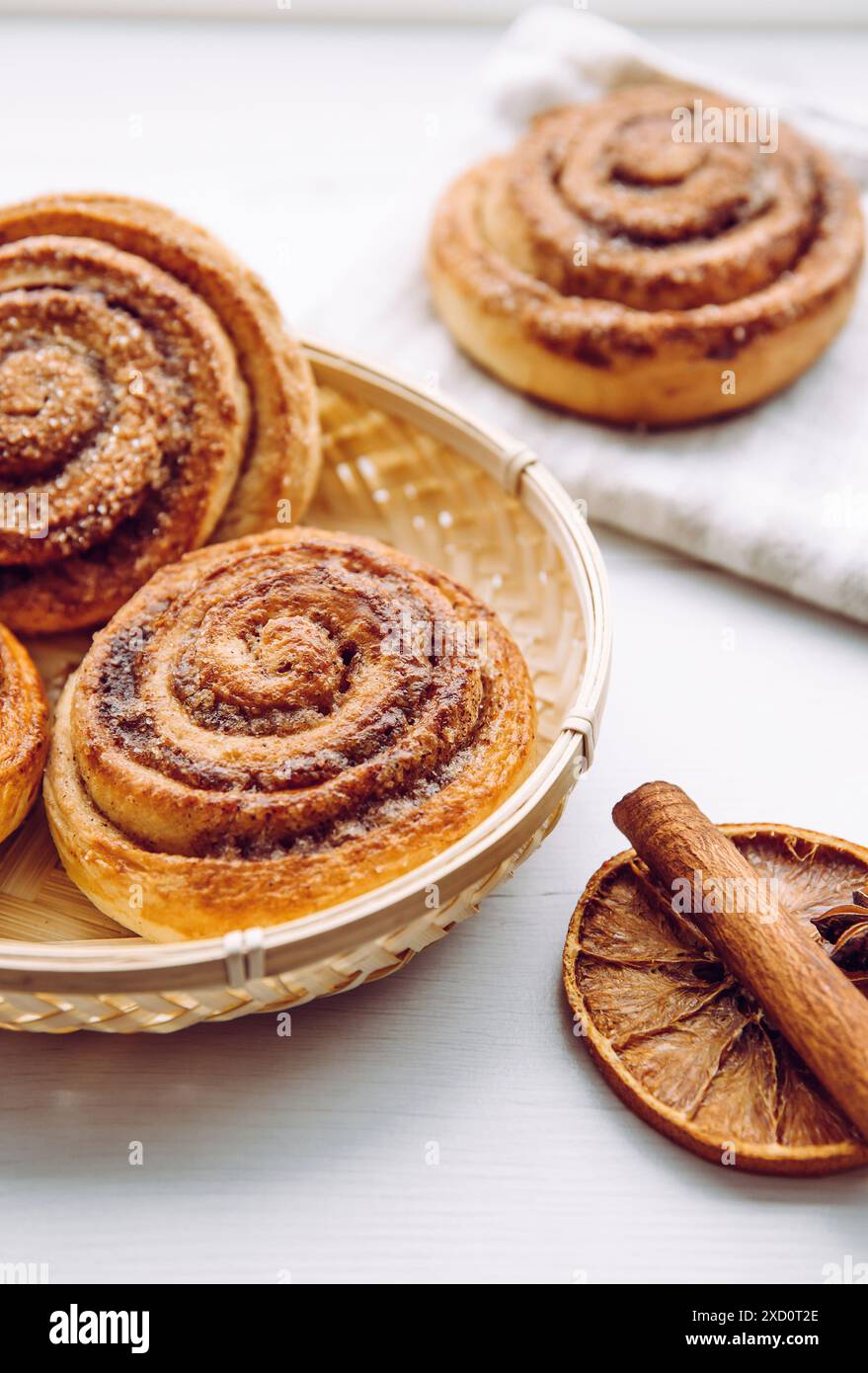 Panini alla cannella appena sfornati con zucchero nel cestino della cucina casalinga su un tavolo bianco, bastoncino alla cannella per la decorazione. Messa a fuoco selettiva. Foto Stock