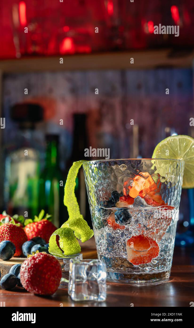 Bere con fragole, mirtilli e lime, serviti in un bicchiere con ghiaccio. Cocktail, rum, vodka, vita notturna, festa e freschezza. Gioia e relax Foto Stock