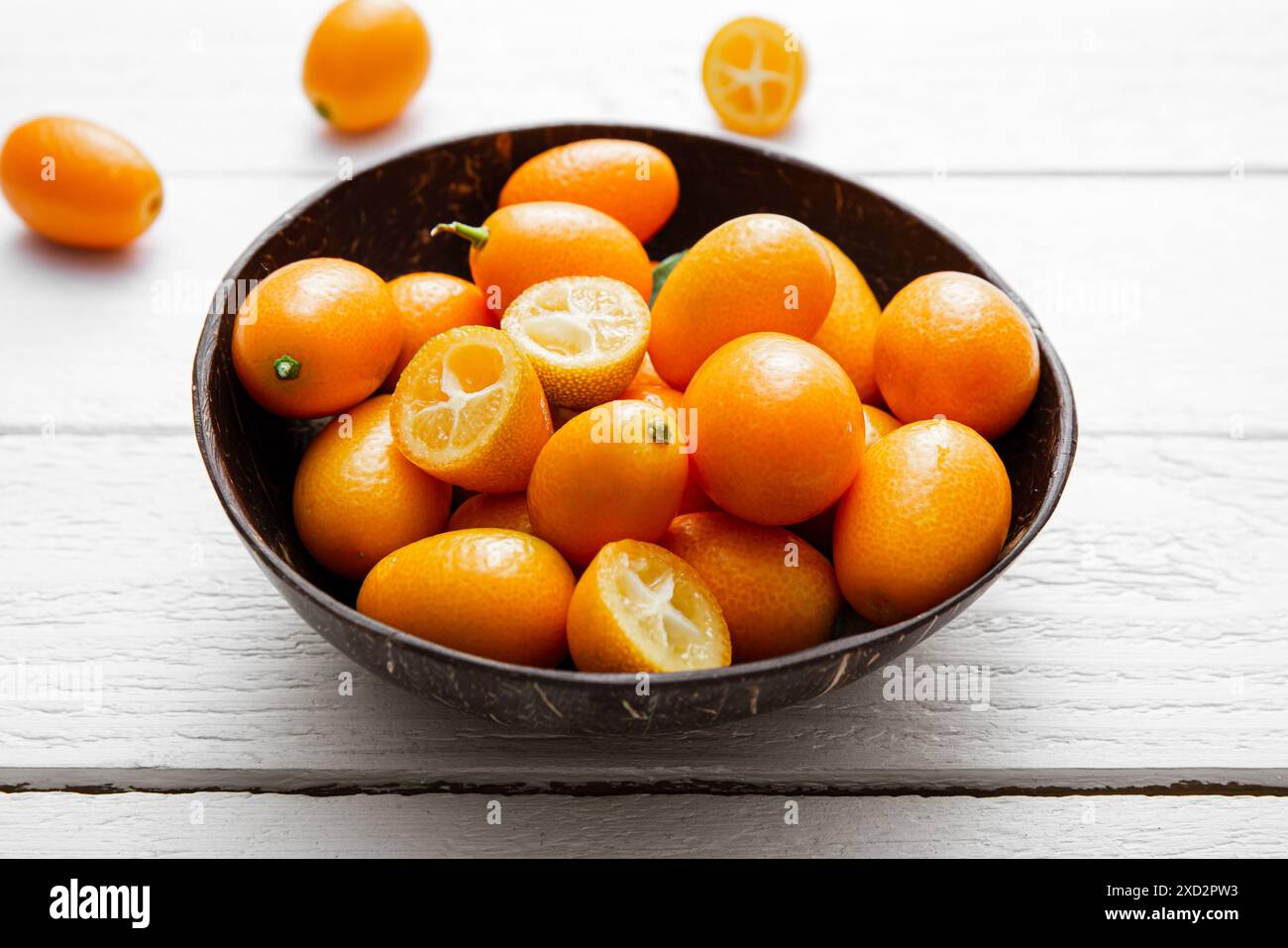 Kumquat o cumquat ( Citrus japonica) all'interno di una ciotola di cocco e su sfondo di legno bianco. Ripresa in studio, luce in studio. Foto Stock