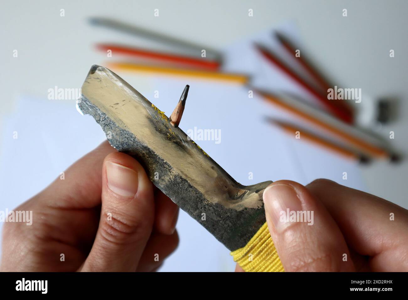 Foto del processo di affilatura delle matite con un coltello da ufficio. Mani umane. Coltello metallico. Sullo sfondo sono presenti dei white paper e delle matite colorate. Creatività, disegno, arte, artista. Foto Stock