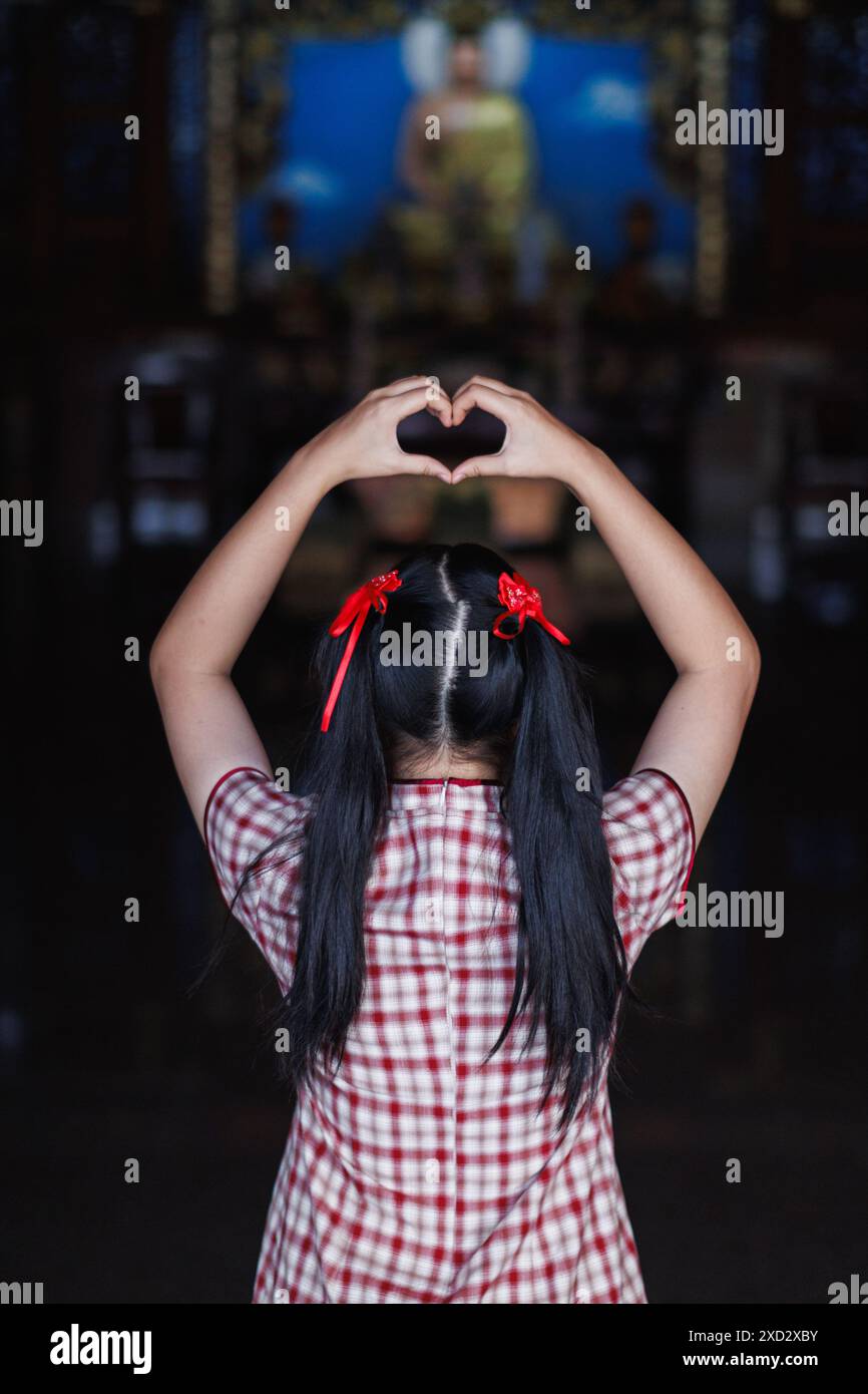 Una giovane donna alza le mani per fare un simbolo del cuore che significa amore e amicizia. Il concetto di using mani per creare un simbolo di cuore rappresenta il mezzo Foto Stock
