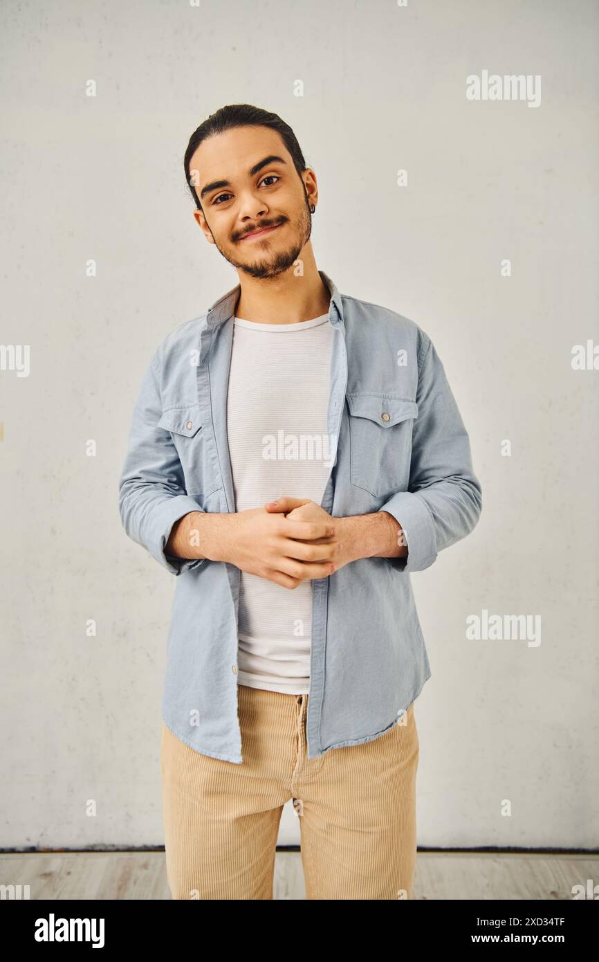 Un giovane uomo con una camicia blu e pantaloni abbronzati posa con fiducia. Foto Stock