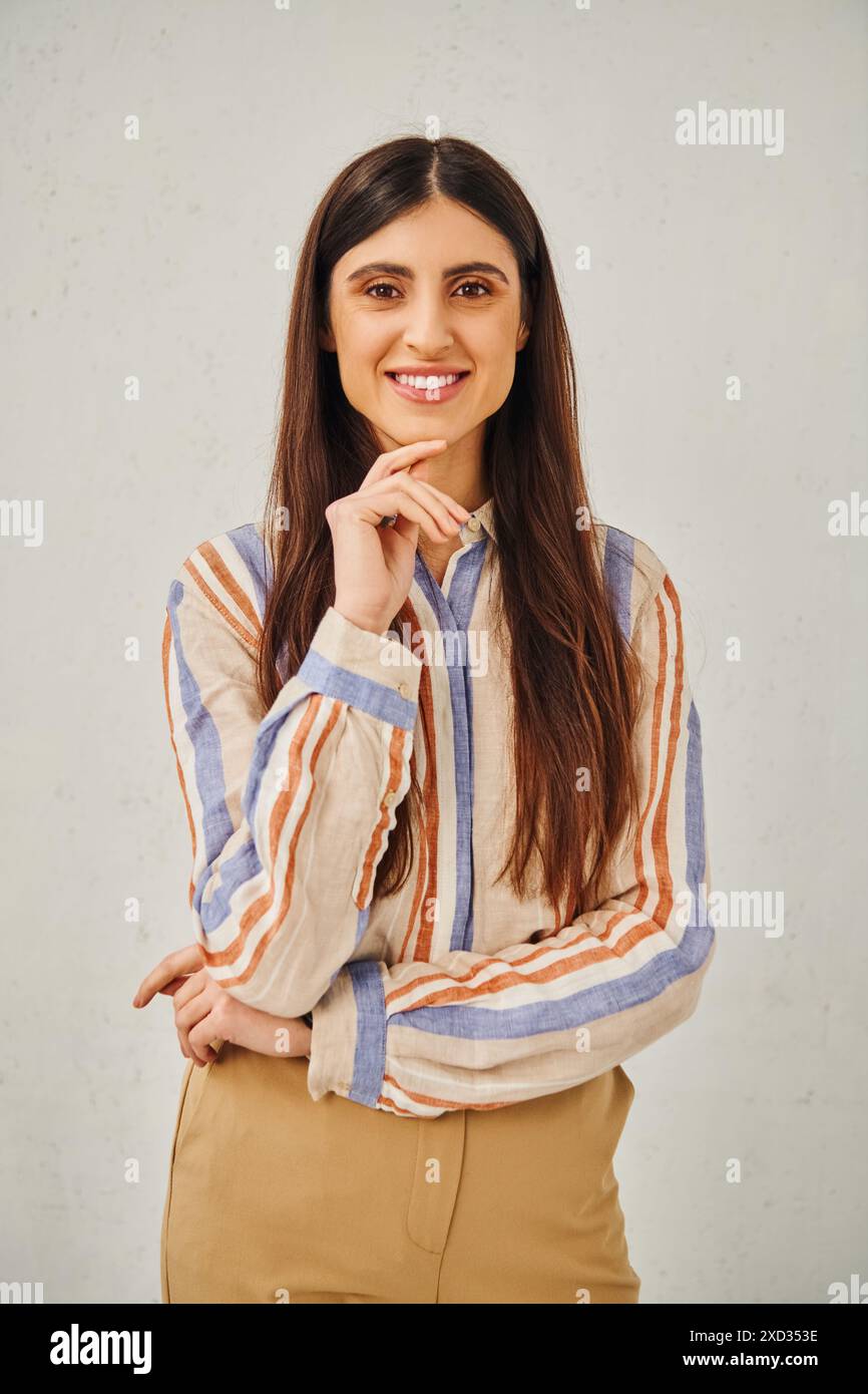Donna elegante in camicia a righe e pantaloni abbronzati che posa per un ritratto. Foto Stock