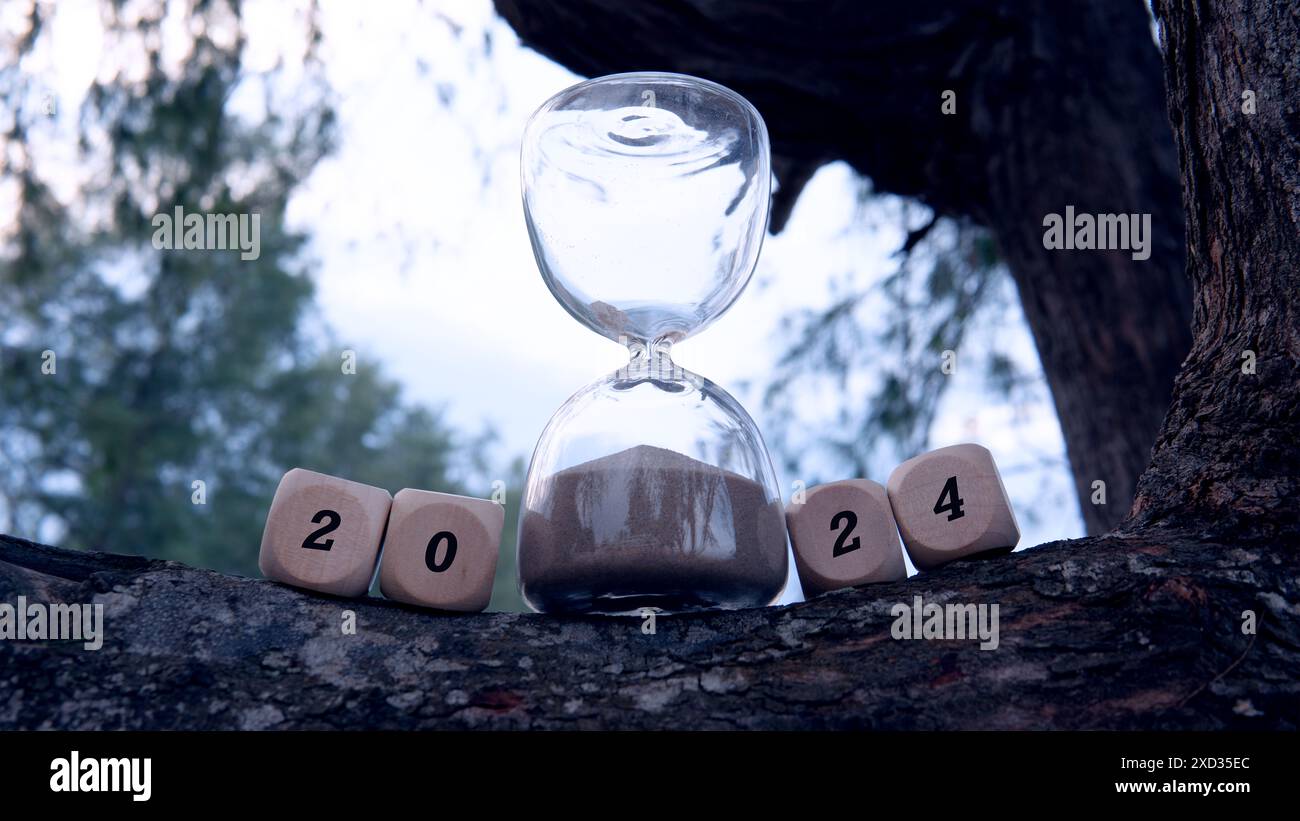 Un'ora di vetro con la sabbia che scende come il tempo volando via per segnare la fine dell'anno 2024. Un cubo di dadi ha l'aspetto di un testo 2024. Foto Stock