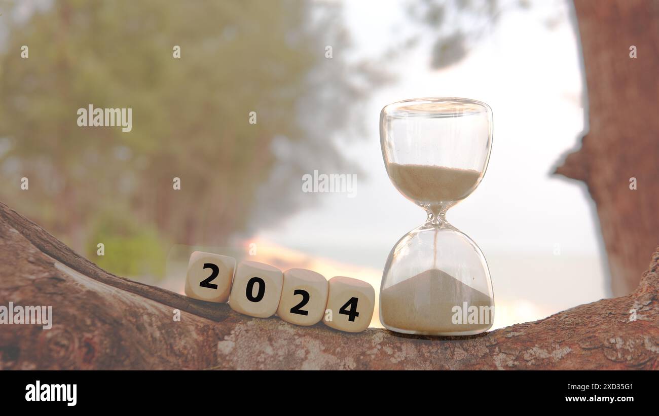 Un'ora di vetro con la sabbia che scende come il tempo volando via per segnare la fine dell'anno 2024. Un cubo di dadi ha l'aspetto di un testo 2024. Foto Stock