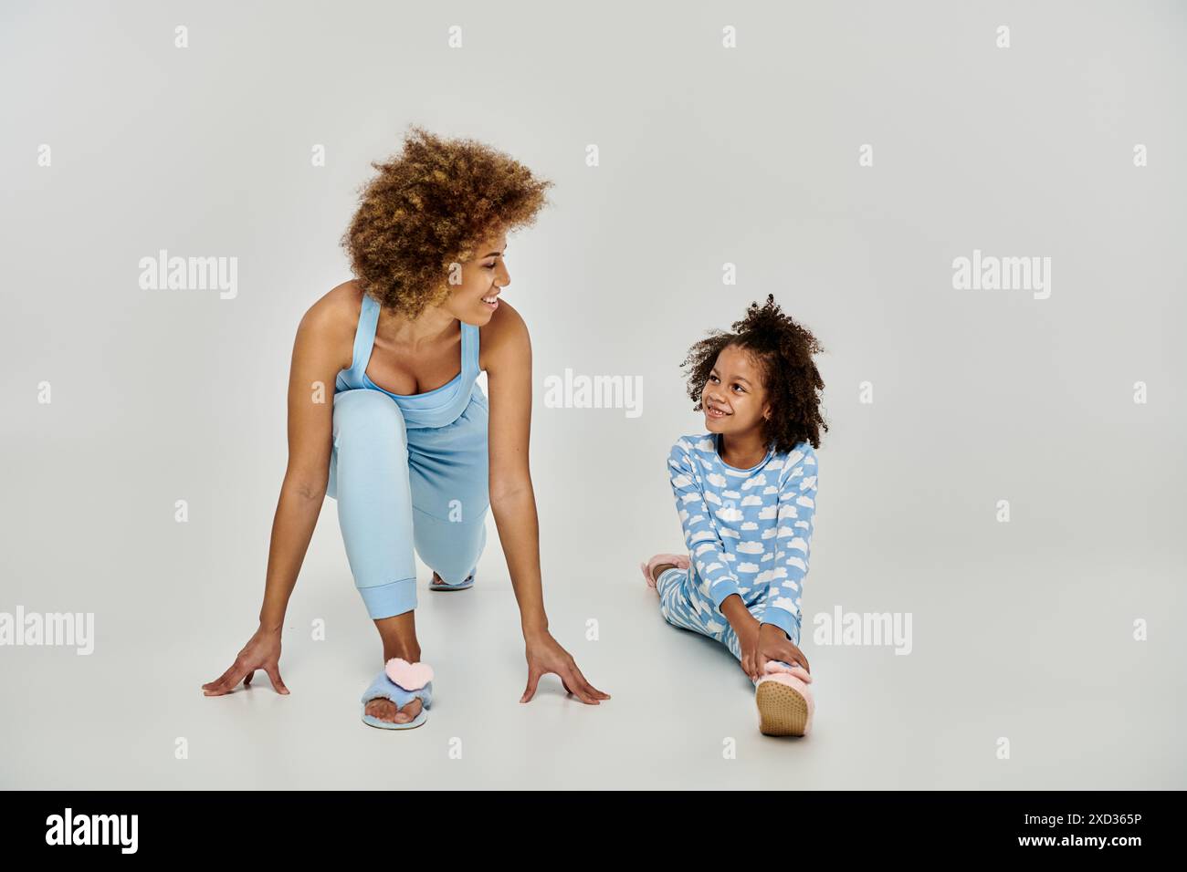 Allegra madre e figlia afroamericana in pigiama che praticano yoga insieme su un tranquillo sfondo bianco. Foto Stock
