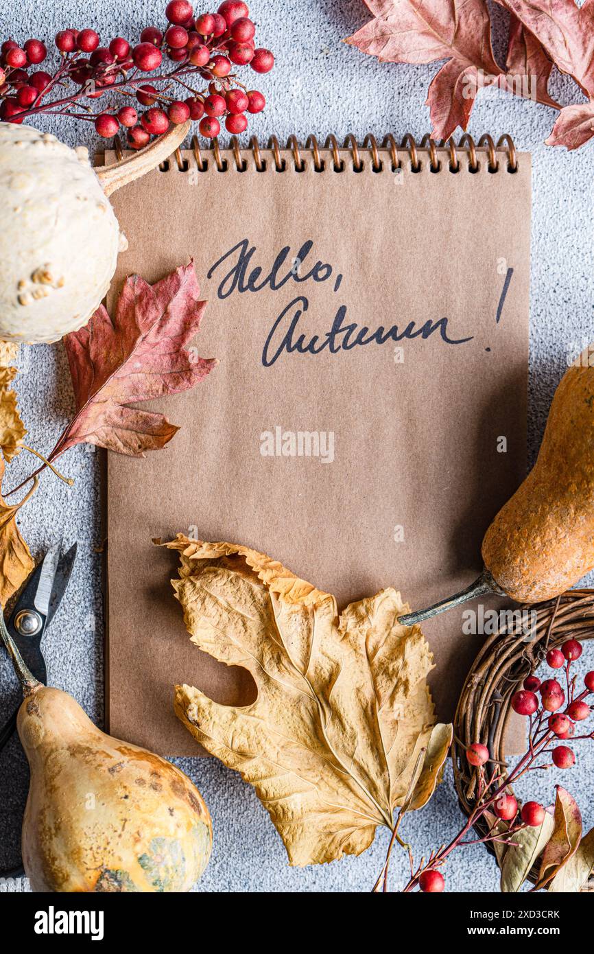 Piatto autunnale in stile artigianale con elementi naturali come foglie secche e buongustai, un notebook con HELLO, messaggio AUTUNNALE e decorazioni stagionali Foto Stock