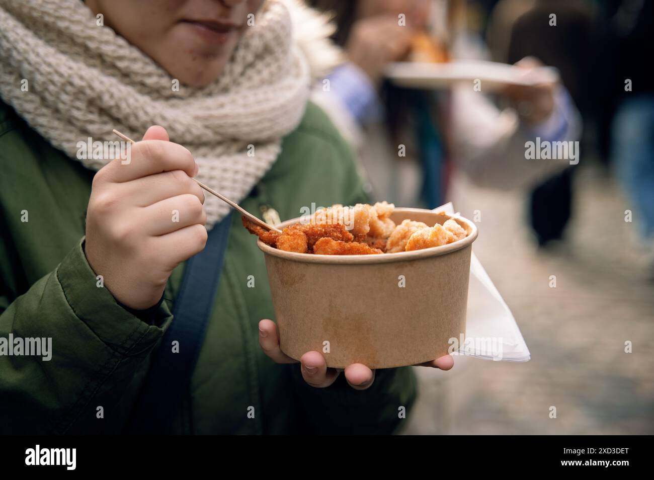 Una persona irriconoscibile e corta che assaggia il cibo di strada da una ciotola di carta in una trafficata strada di Londra. Foto Stock