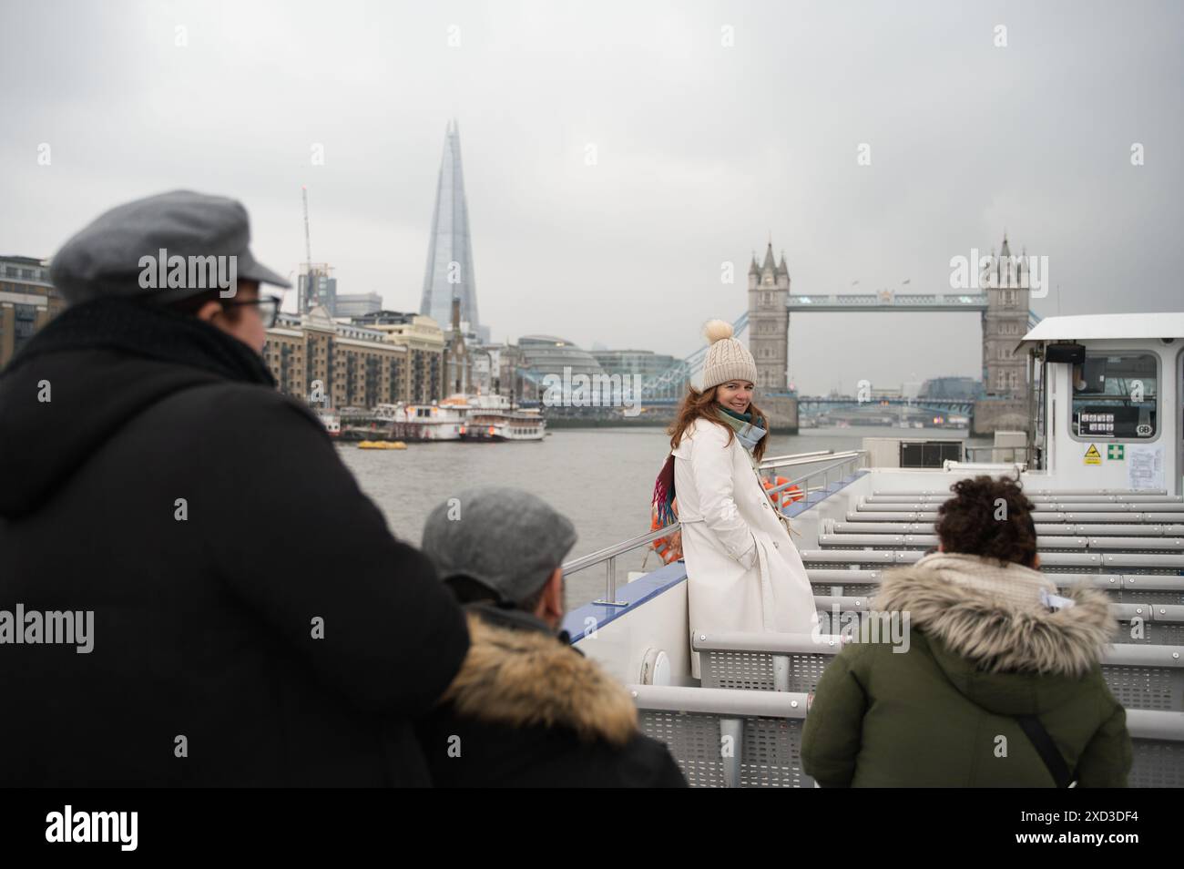 Una famiglia gioiosa che si imbarca in una crociera sul fiume con iconici monumenti di Londra sullo sfondo in una giornata nuvolosa. Foto Stock