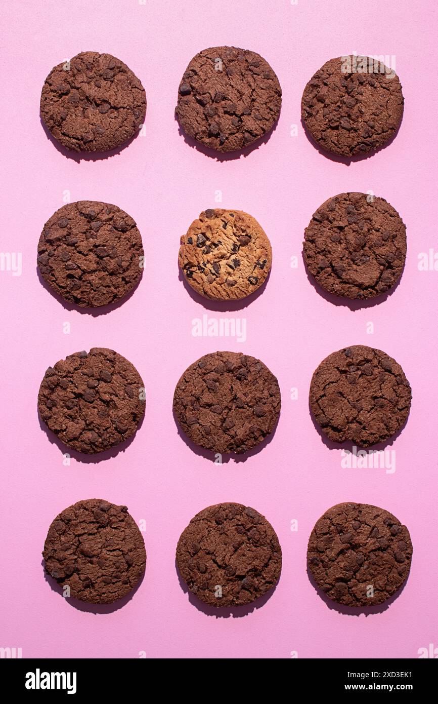 Fotografie piatte di dodici biscotti a goccia di cioccolato doppi disposti su un vivace sfondo rosa Foto Stock