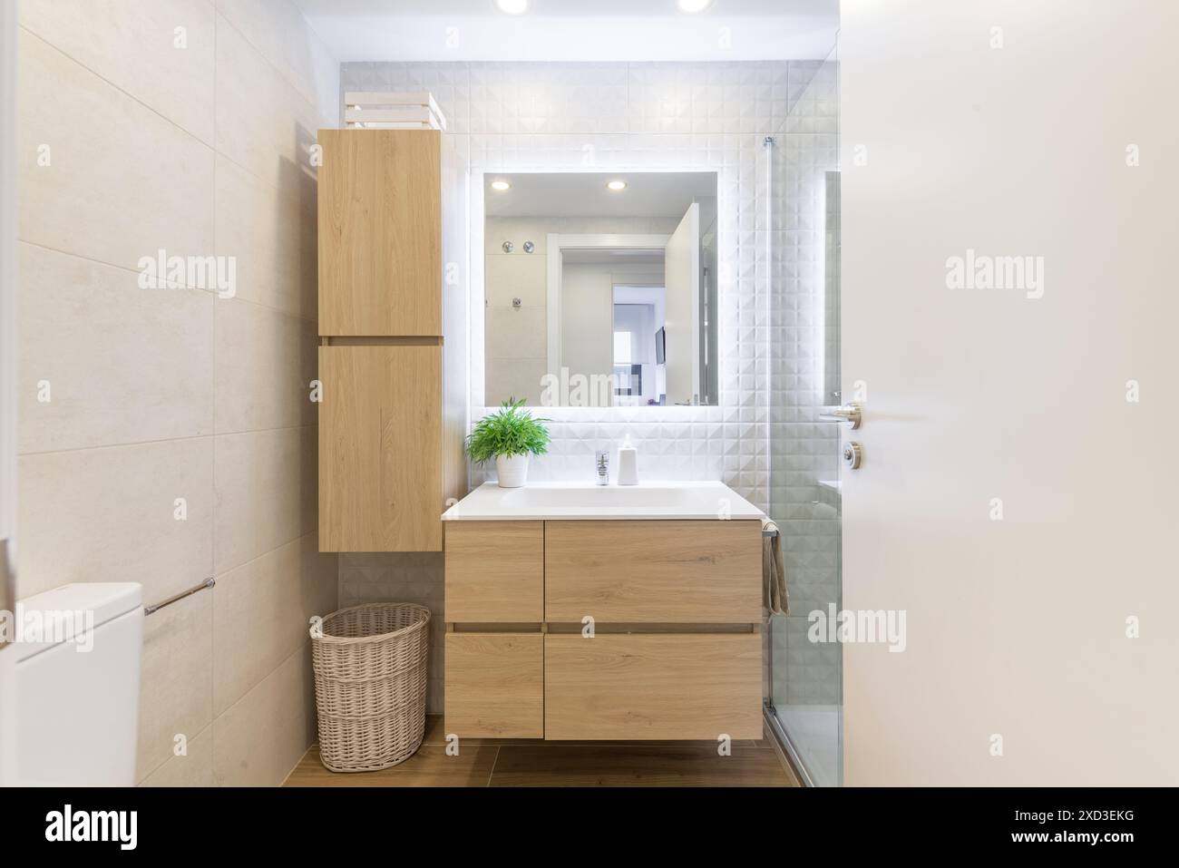 Questa immagine mostra un moderno interno del bagno caratterizzato da un lavandino in legno, piastrelle di colore chiaro e un design minimalista. Luminosa e ariosa, include Foto Stock
