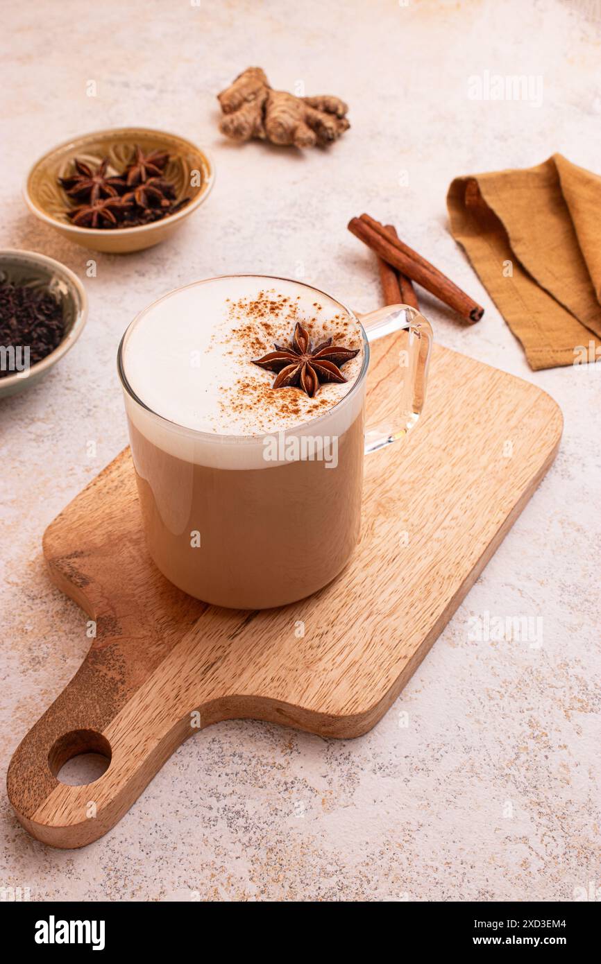 Dall'alto, delizioso chai latte con schiuma cremosa su una tavola di legno circondata da anice stellato, bastoncini di cannella, zenzero fresco, foglie di tè, un vasetto di latte A. Foto Stock