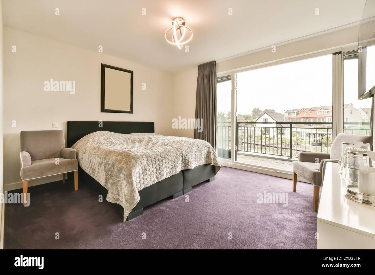 Una camera da letto con moquette viola e un letto davanti ad una porta scorrevole in vetro che conduce ad un balcone Foto Stock