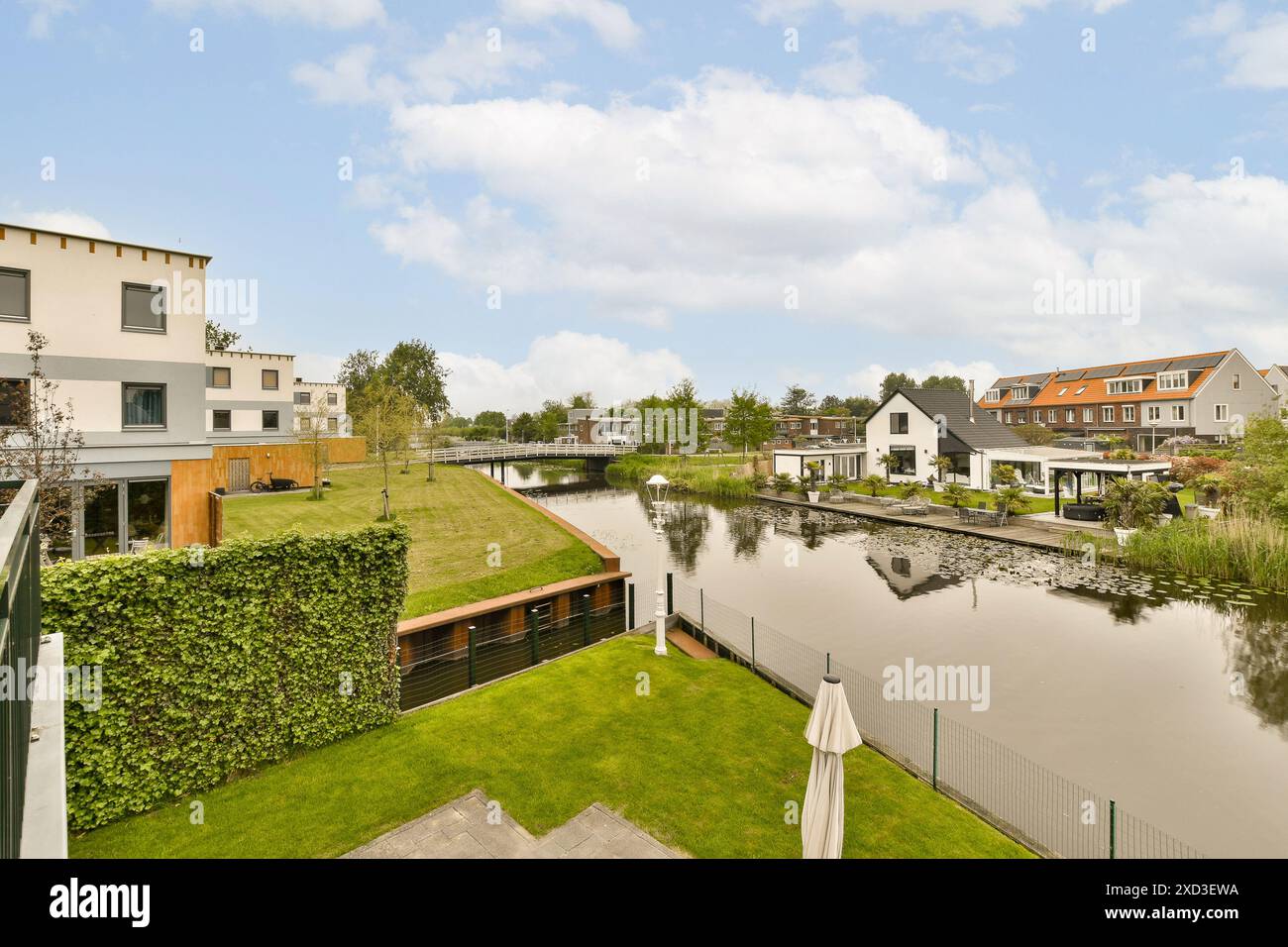 Una vista panoramica di un tranquillo canale fiancheggiato da case moderne e lussureggiante vegetazione. Questo ambiente pittoresco offre acque cristalline, prati vivaci e sereni Foto Stock