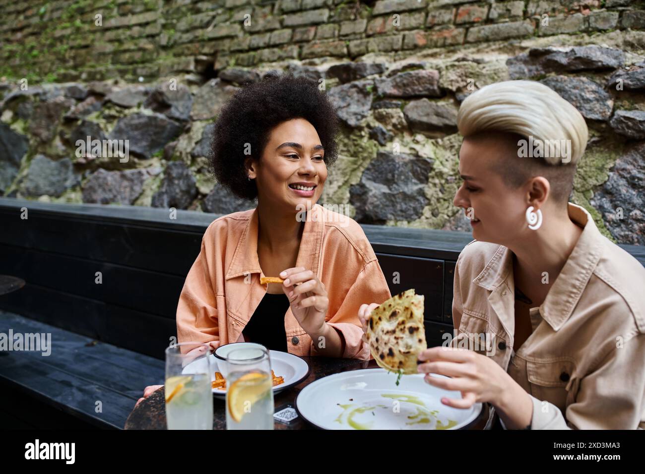 Due donne diverse e belle si siedono a un tavolo e mangiano felicemente pizza in un accogliente bar. Foto Stock