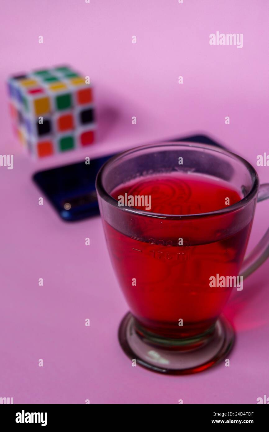 Foto di bevanda rossa, smartphone blu e Rubik su sfondo rosa Foto Stock