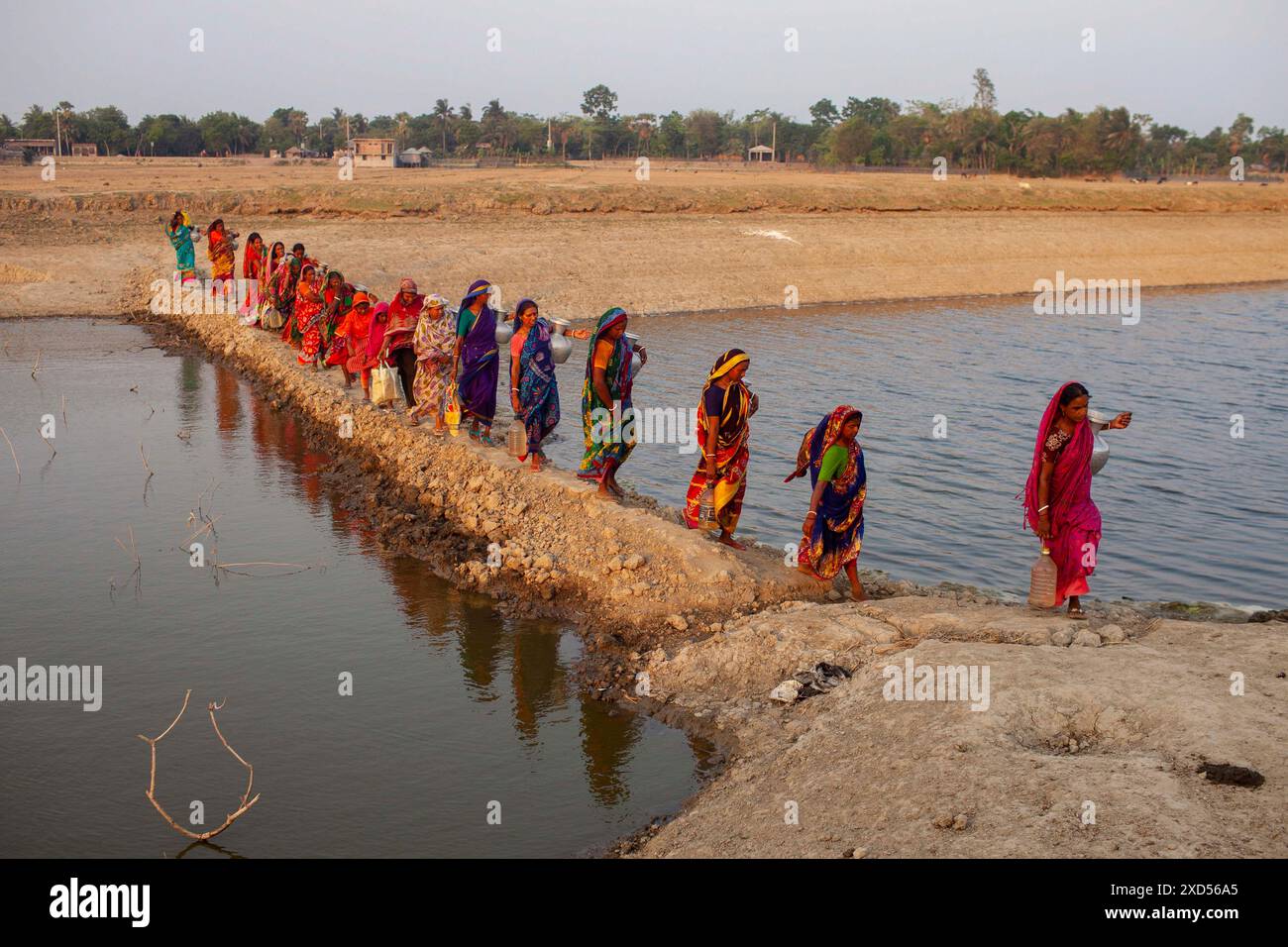 20 giugno 2024, Dacca, Dacca, Bangladesh: Le donne del Bangladesh trasportano acqua potabile dopo averla raccolta da una fonte di acqua dolce, camminando molto per raccogliere acqua potabile nella zona costiera di Khulna, Bangladesh. Secondo una ricerca dell'American Geophysical Union, l'innalzamento del livello del mare, che sta influenzando la disponibilità di acqua potabile pulita, causerà la migrazione di circa 1,3 milioni di persone in tutto il paese entro il 2050. Una combinazione di inondazione delle maree, inondazione delle tempeste e intrusione di acqua salata sta portando a un aumento della salinità nelle acque sotterranee e nelle acque dolci del po Foto Stock