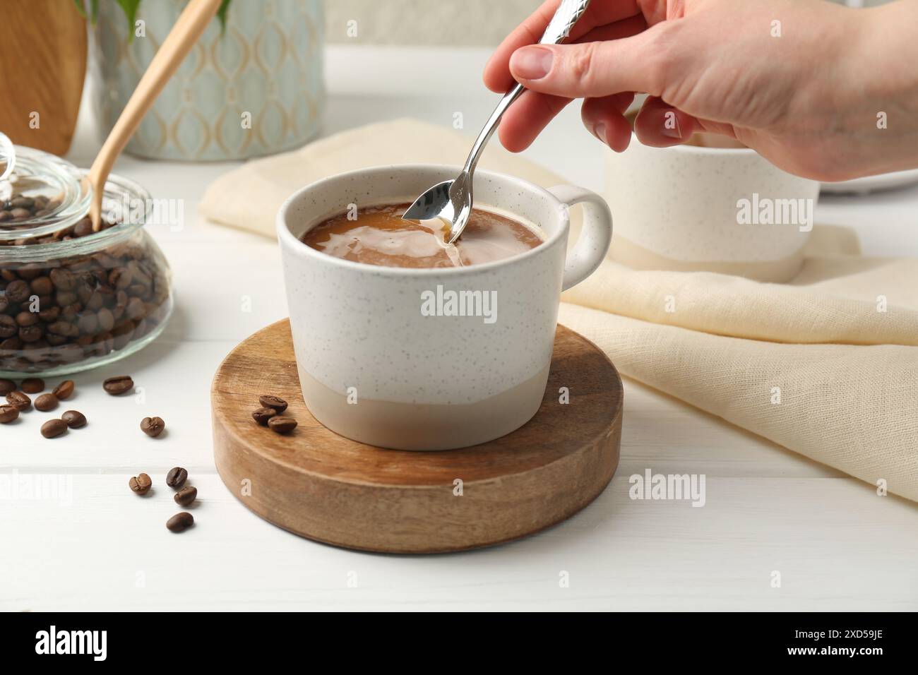 Donna che mescola il caffè con un cucchiaio al tavolo di legno bianco, primo piano Foto Stock