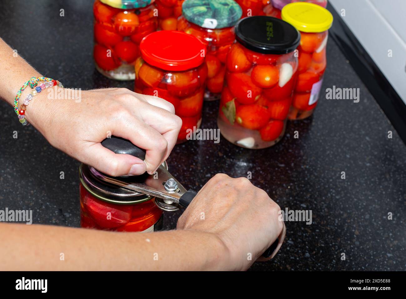 Una donna sale pomodori rossi maturi in vasetti di vetro, arrotolando il coperchio di metallo con una macchina. Prepariamo le verdure per l'inverno. Foto Stock