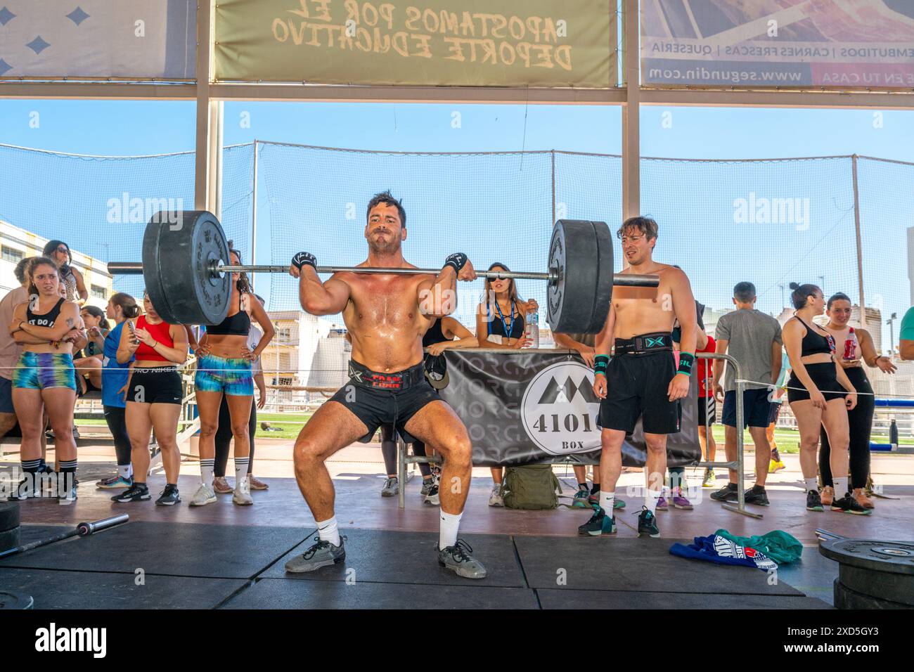 Atleti che praticano il sollevamento pesi in un'intensa competizione CrossFit ambientata a Siviglia, Spagna. La folla guarda e tifa i partecipanti. Foto Stock