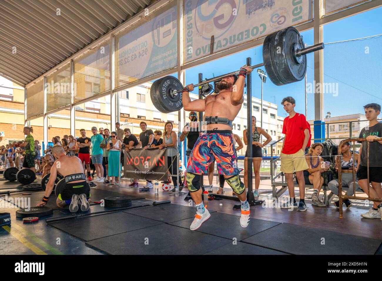 Atleti che praticano il sollevamento pesi in un'intensa competizione CrossFit ambientata a Siviglia, Spagna. La folla guarda e tifa i partecipanti. Foto Stock