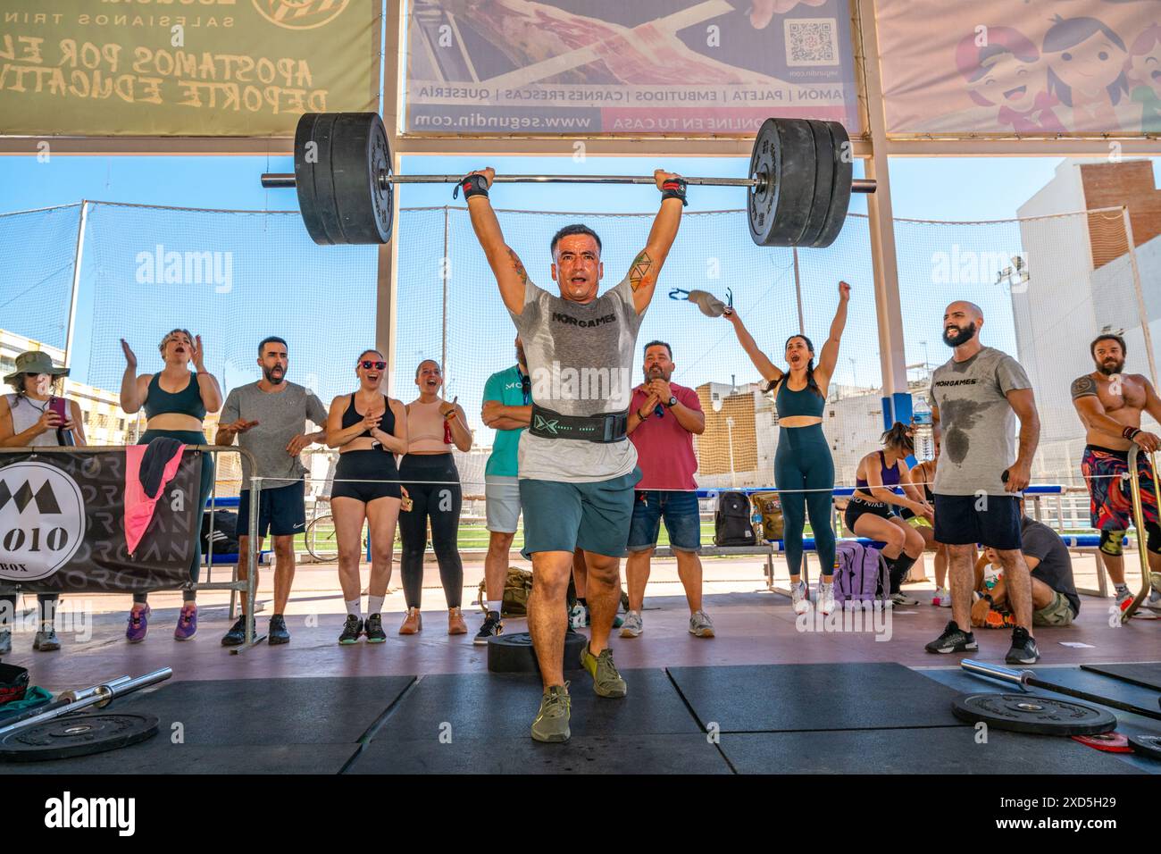 Atleti che praticano il sollevamento pesi in un'intensa competizione CrossFit ambientata a Siviglia, Spagna. La folla guarda e tifa i partecipanti. Foto Stock