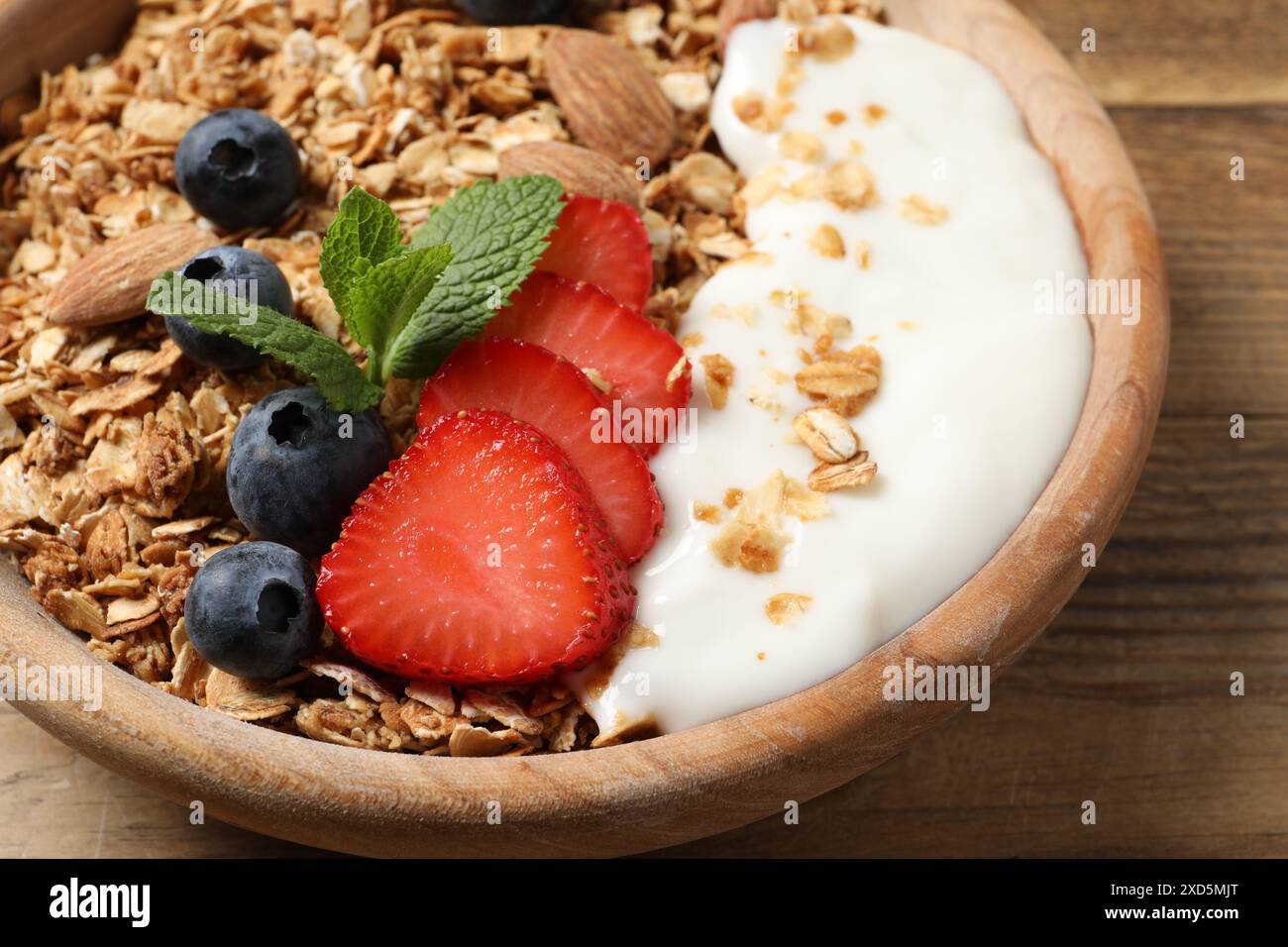 Gustose muesli con frutti di bosco, mandorle e yogurt in ciotola su un tavolo di legno, primo piano Foto Stock