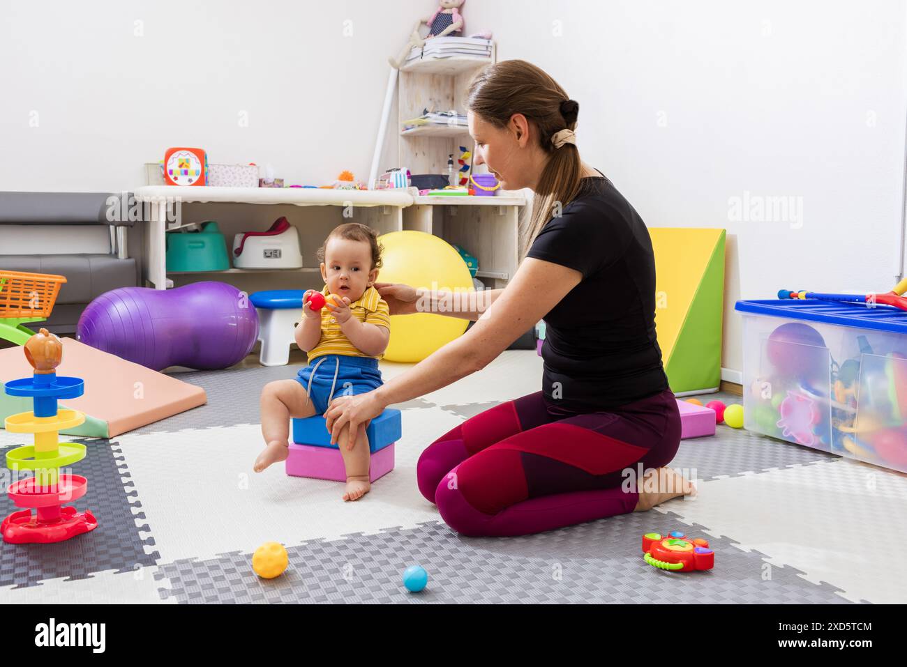 Fisioterapista che aiuta il bambino durante l'esercizio di sviluppo delle capacità motorie in una clinica di riabilitazione. Intervento nella prima infanzia con terapia fisica Foto Stock