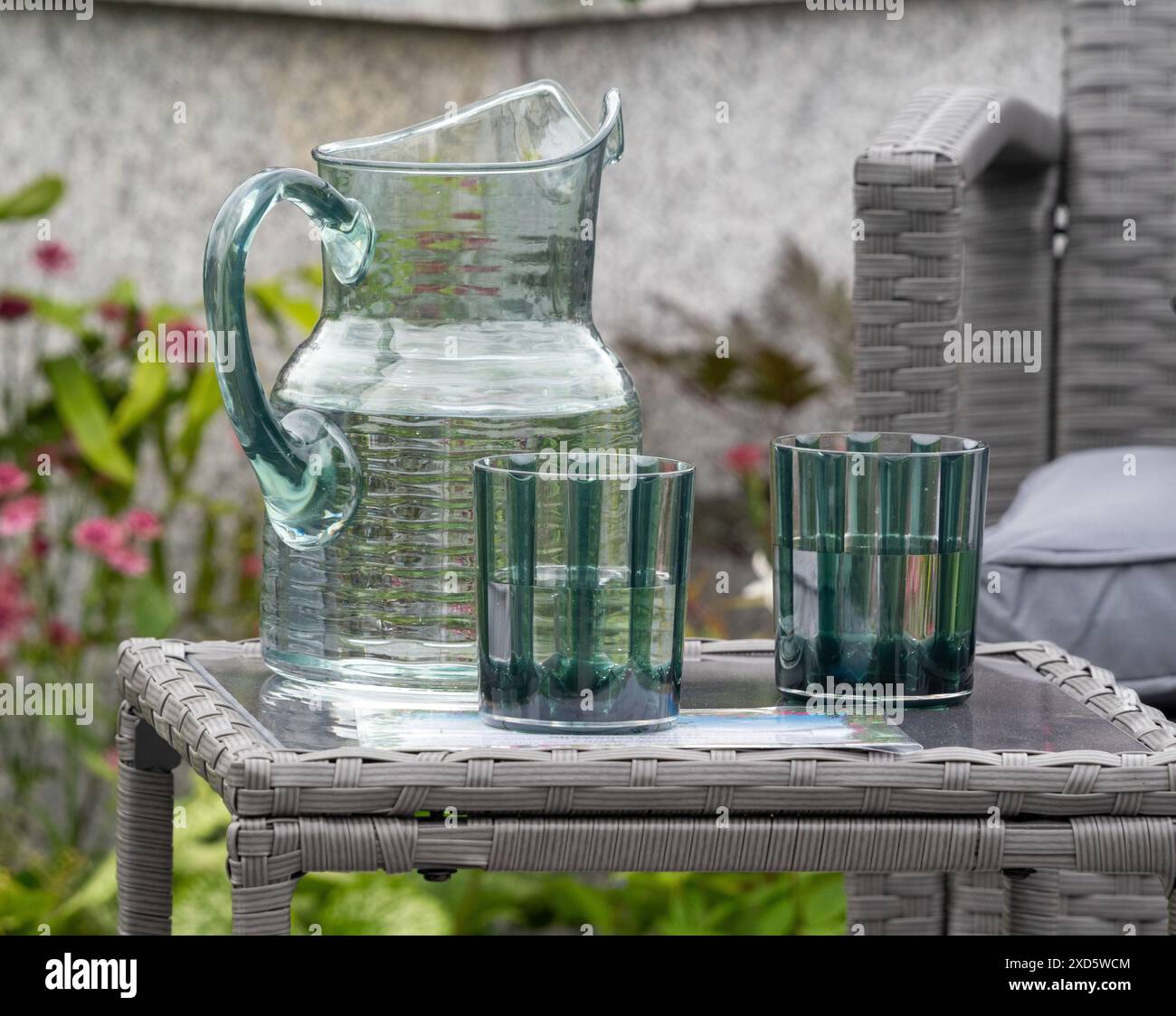 Caraffa di vetro e due bicchieri su un tavolo da giardino in stile rattan grigio. Foto Stock