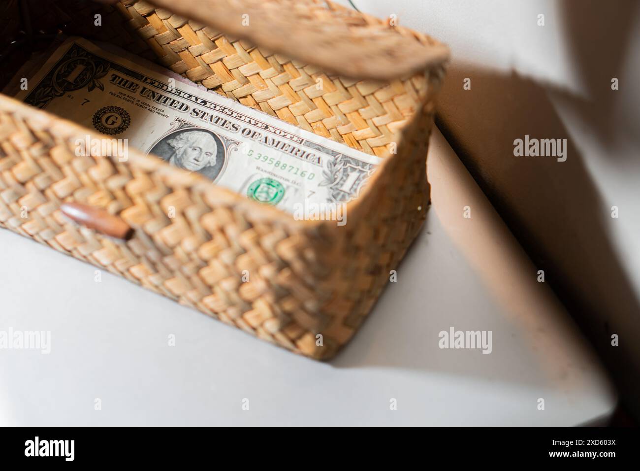 Un cestino in tessuto contenente una banconota da un dollaro, collocato su una superficie bianca. Foto Stock