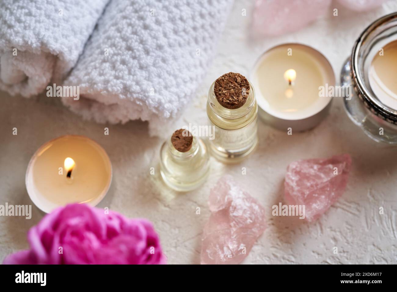 Bottiglie di olio essenziale aromaterapico con pietre di quarzo rosa, fiori di rosa e asciugamani termali su sfondo bianco Foto Stock