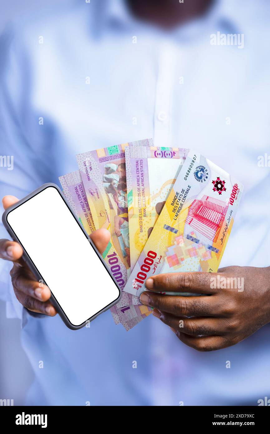 Persona di colore con appunti in franco CFA dell'Africa centrale e con schermo vuoto che mostra il telefono alla fotocamera. Tenere a mano banconote in valuta dell'Africa centrale, Foto Stock