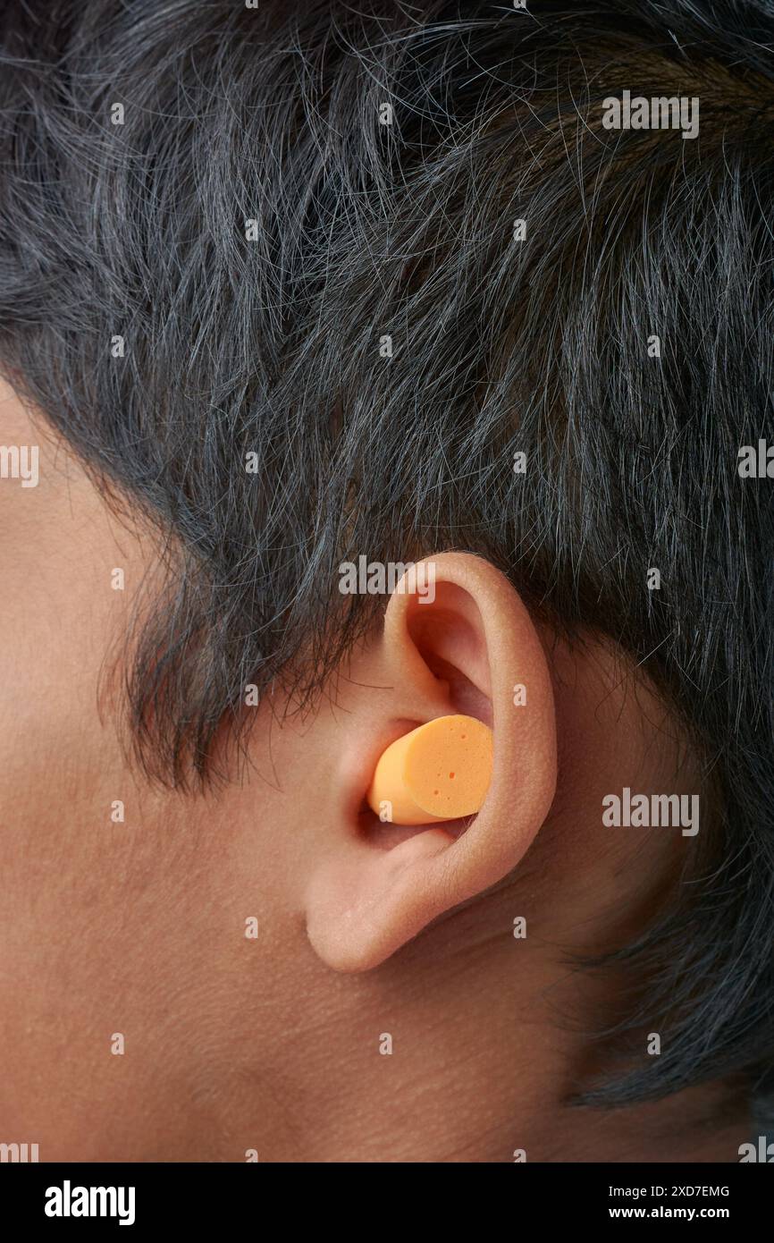 inserti auricolari monouso in morbida schiuma espandibile inseriti nell'orecchio, indossando una protezione per l'udito monouso senza filo e comoda per l'uso sul posto di lavoro, concerti Foto Stock