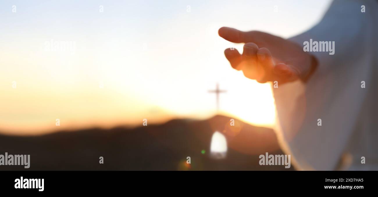 Mani di Gesù risorto dalla tomba e sfondo luminoso, cielo e croce amore e concetto di salvezza Foto Stock