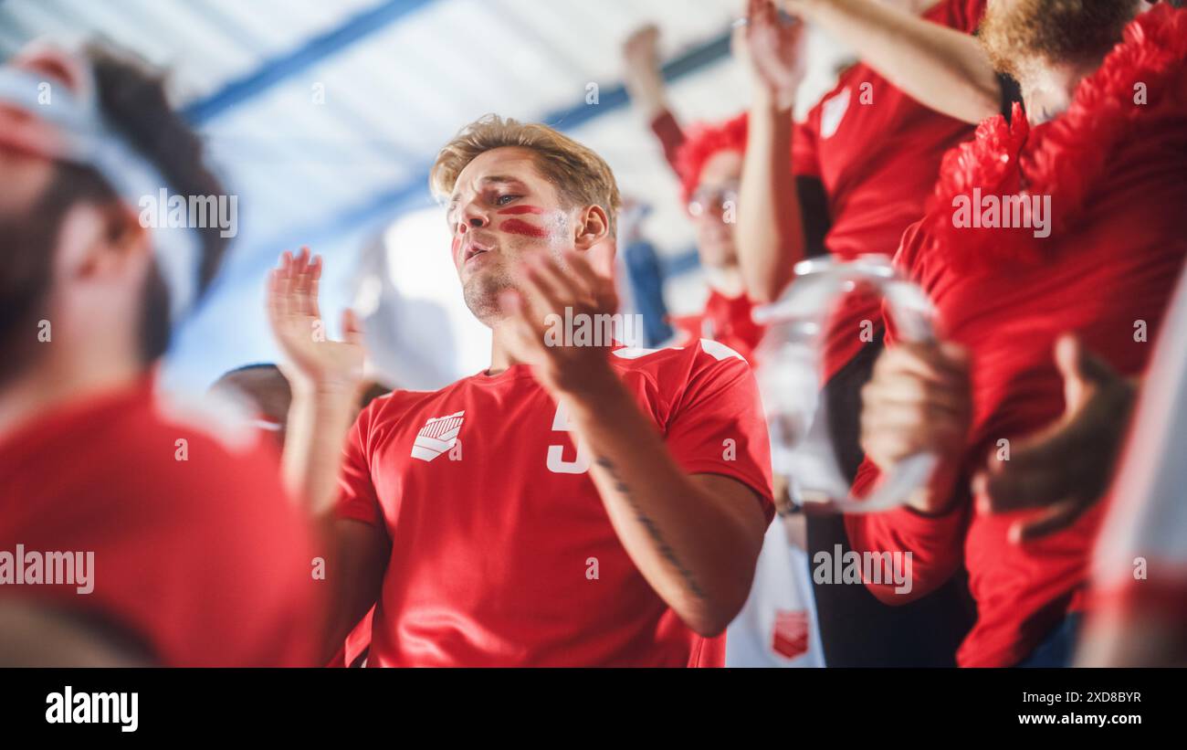 Grande evento dello stadio sportivo: Intenso tifo dell'uomo caucasico, Whistling. Una folla di tifosi con Painted Faces Cheer, grida per la squadra di calcio rossa per vincere. I tifosi festeggiano segnando un gol, Championship Victory Foto Stock