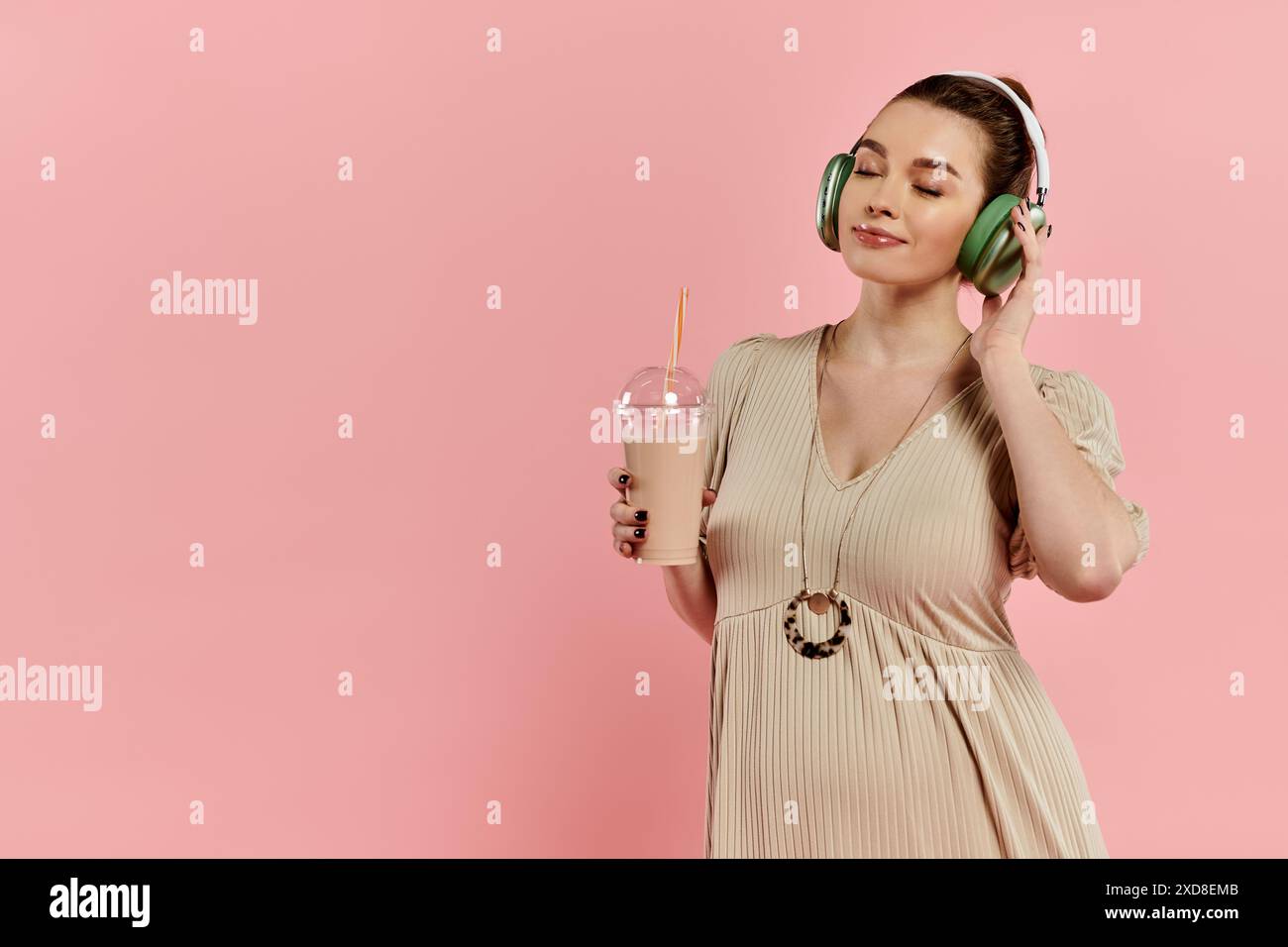 Una giovane donna incinta ascolta con gioia la musica attraverso le cuffie mentre tiene in mano un drink. Foto Stock