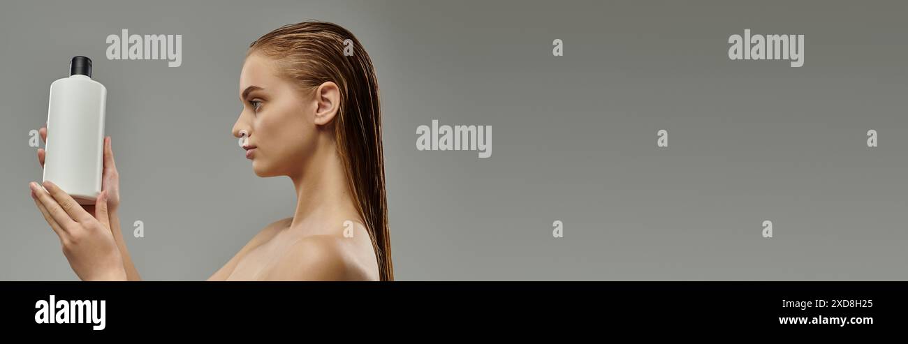 Una giovane donna tiene in mano una bottiglia di prodotto per la cura dei capelli, mostrando la sua routine di bellezza con i capelli bagnati. Foto Stock