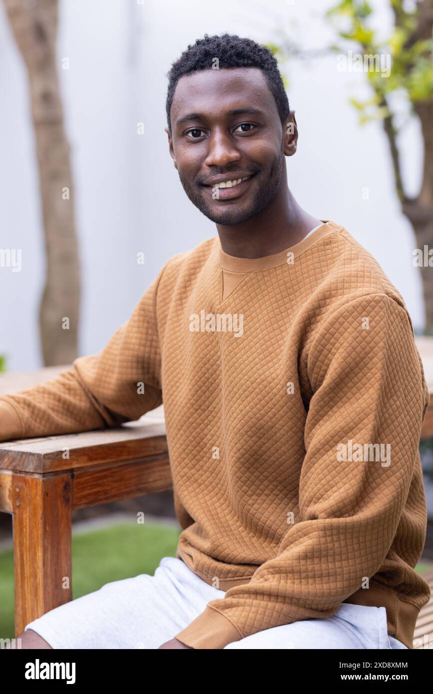 Uomo in abiti informali seduto a un tavolo di legno, sorridente alla macchina fotografica Foto Stock