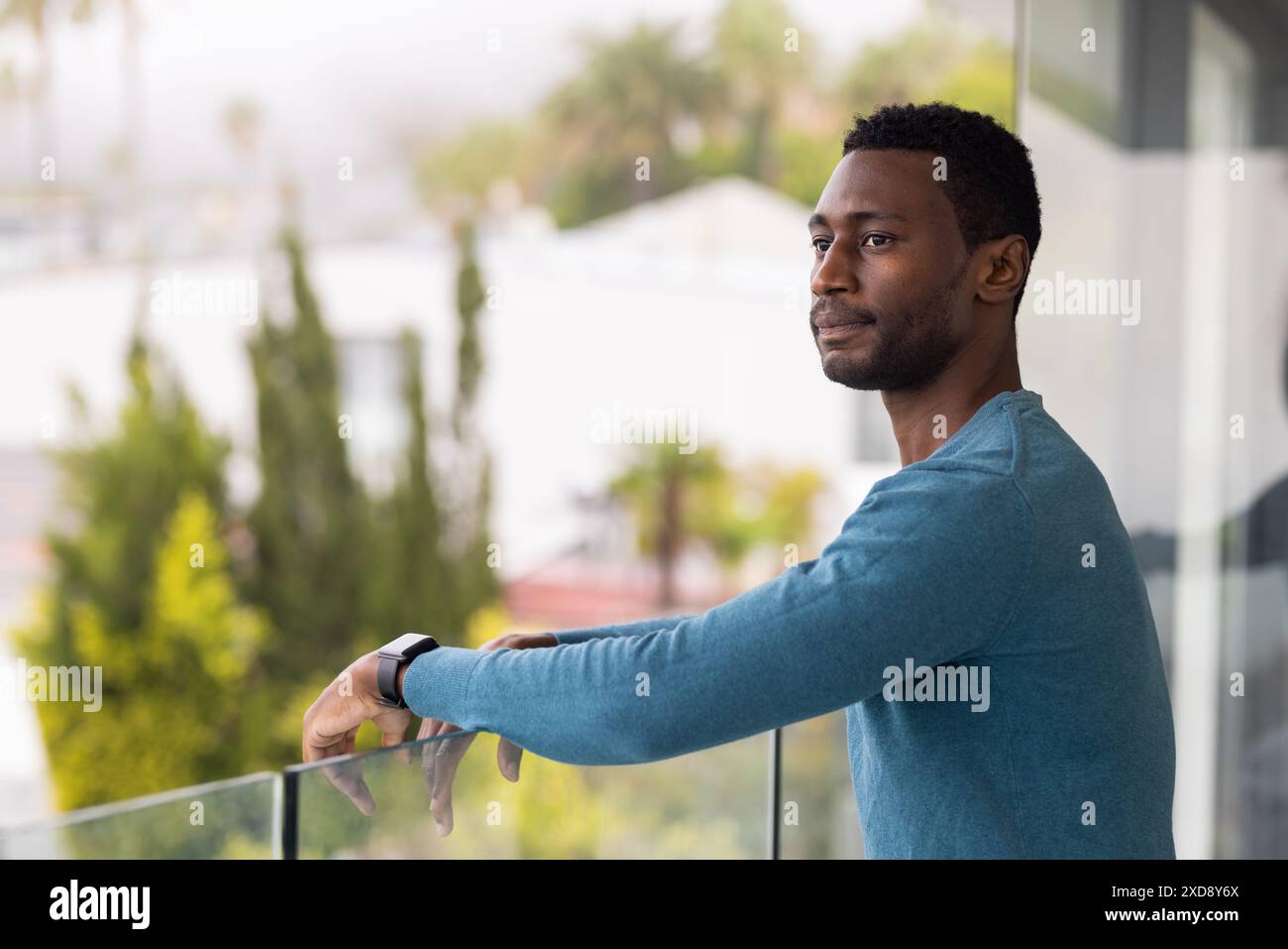 In piedi sul balcone, uomo afroamericano con maglione blu che guarda in lontananza Foto Stock