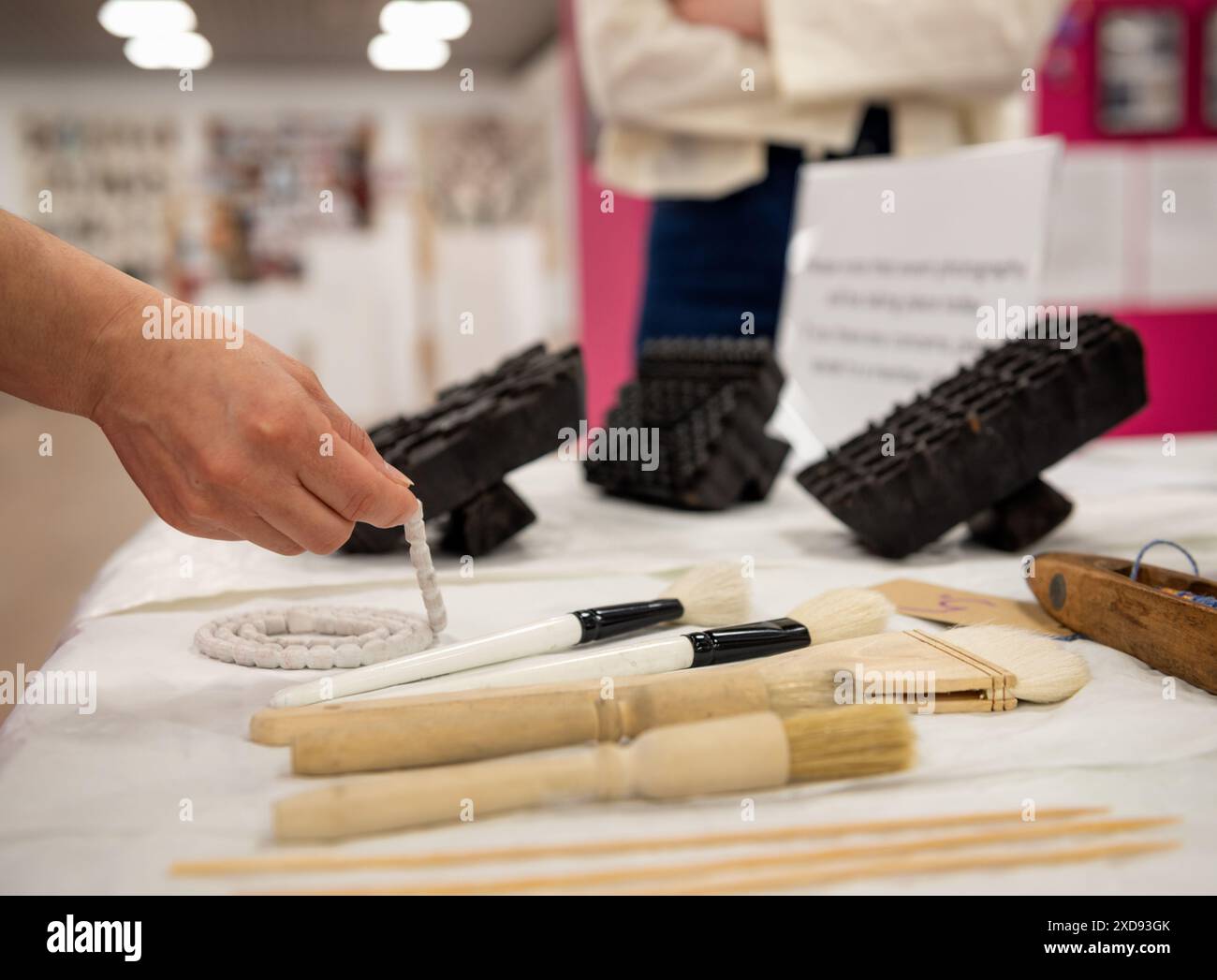 Una mano tiene una spazzola accanto a un tessuto del museo in una mostra di conservazione degli scialli Foto Stock