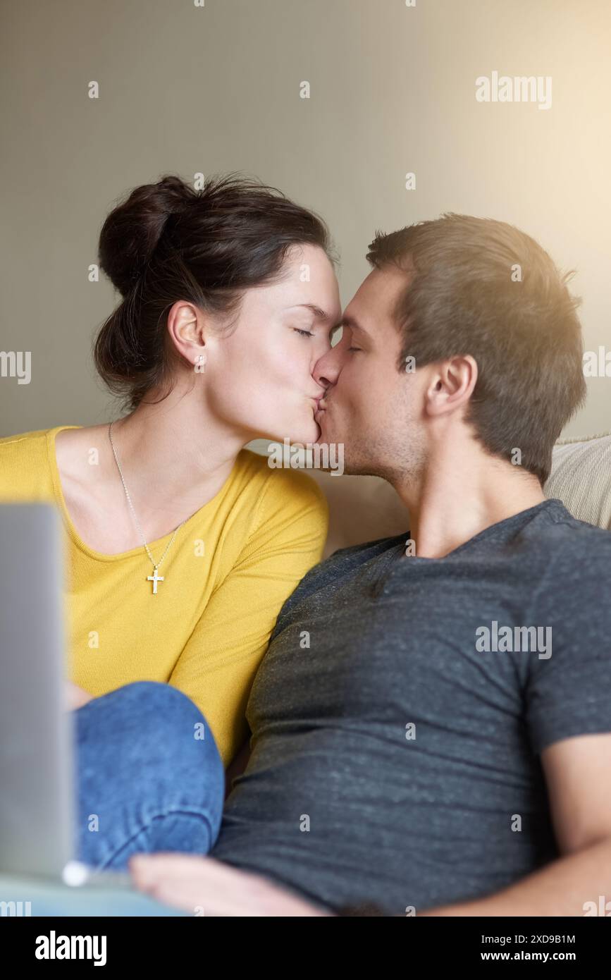 Coppia, baci e laptop sul divano con amore o legame per romanticismo con video in streaming, commedie e online. Uomo, donna e relax insieme a casa Foto Stock