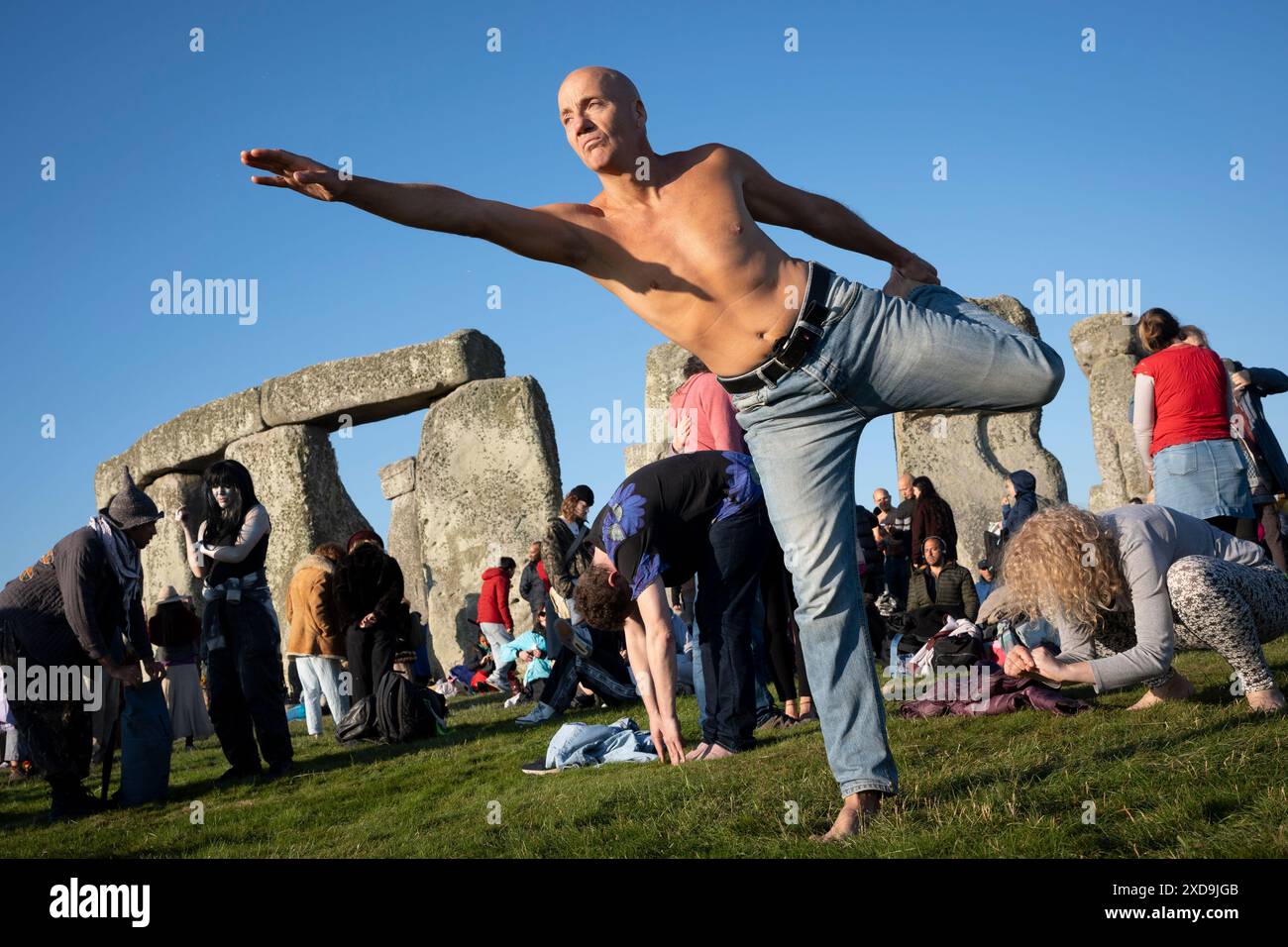 Una classe di yoga di rivelatori spiritualmente mentali celebrano il solstizio d'estate (metà estate e giorno più lungo) presso le antiche pietre tardo-neolitiche di Stonehenge, il 21 giugno 2024, nel Wiltshire, Inghilterra. Il solstizio d'estate è il giorno più lungo dell'emisfero settentrionale e la notte più breve dell'anno, quando l'asse terrestre è inclinato nel punto più vicino al sole e i pagani dicono che l'antico monumento è un luogo sacro che collega la Terra, la Luna, il Sole e le stagioni. Stonehenge è stata costruita in tre fasi tra il 3.000 a.C. e il 1.600 a.C. Stonehenge è di proprietà dell'English Heritage, che dice lo fossero 15.000 visitatori Foto Stock