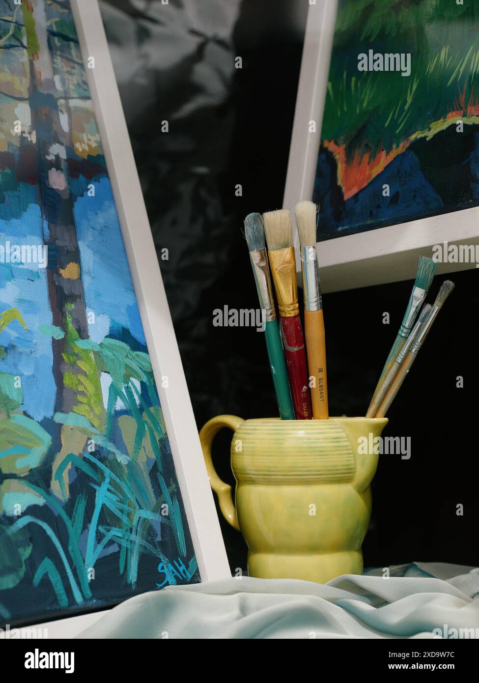 Un'esposizione artistica di dipinti e pennelli in una tazza gialla. Foto Stock