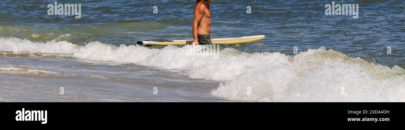 Surfista che entra in acqua accanto alla sua tavola da surf gialla pronto a remare verso le onde per fare surf. Foto Stock