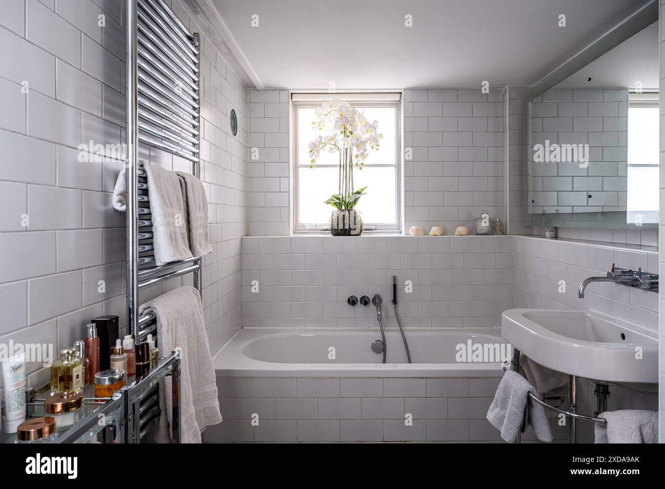 Bagno con piastrelle bianche in orchidea retroilluminata con radiatore montato a parete in una casa scolastica vittoriana convertita alla fine del XIX secolo, Battersea, Londra, Regno Unito Foto Stock