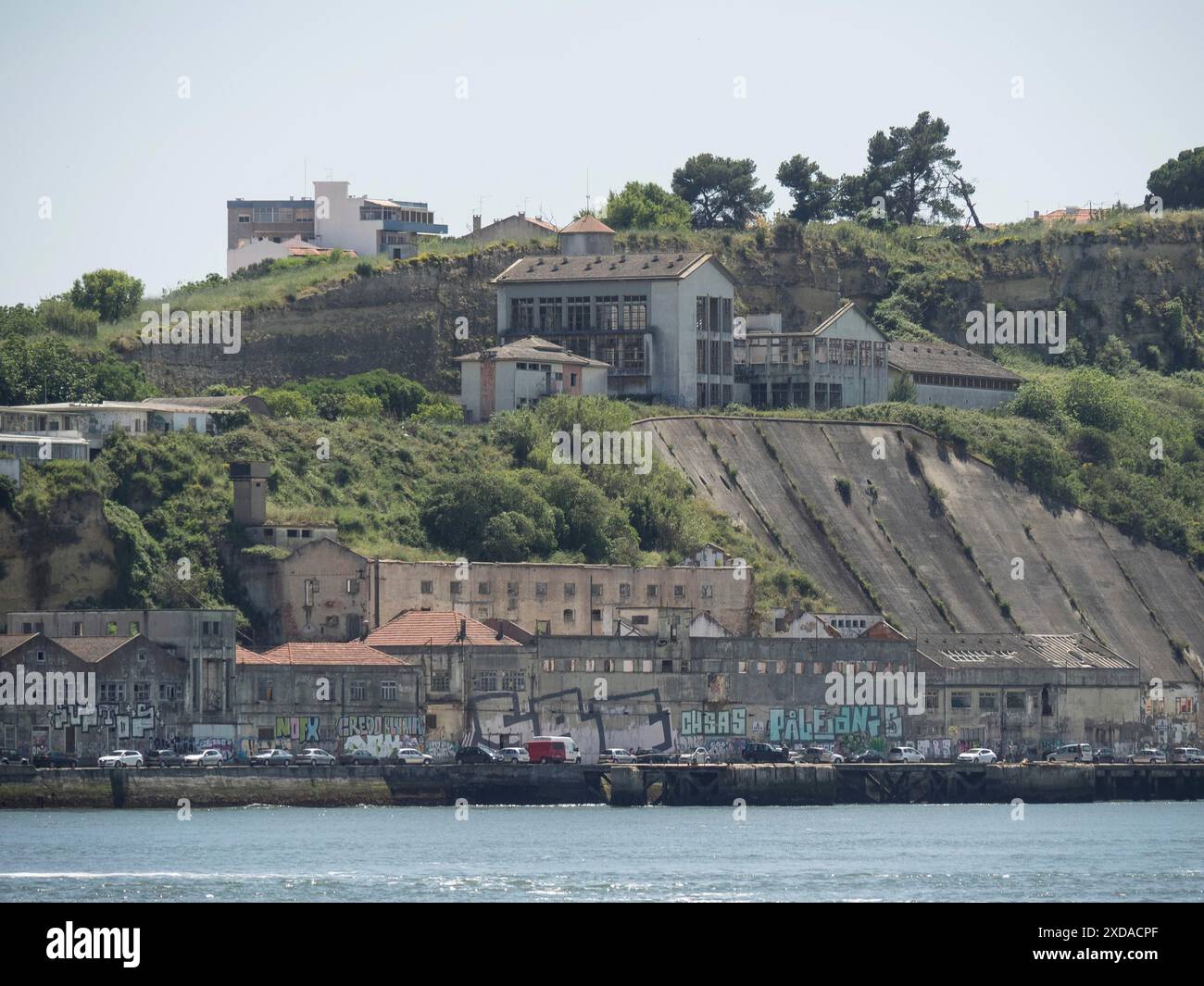 Edifici industriali abbandonati su una collina boscosa sotto un cielo limpido, lisbona, portogallo Foto Stock