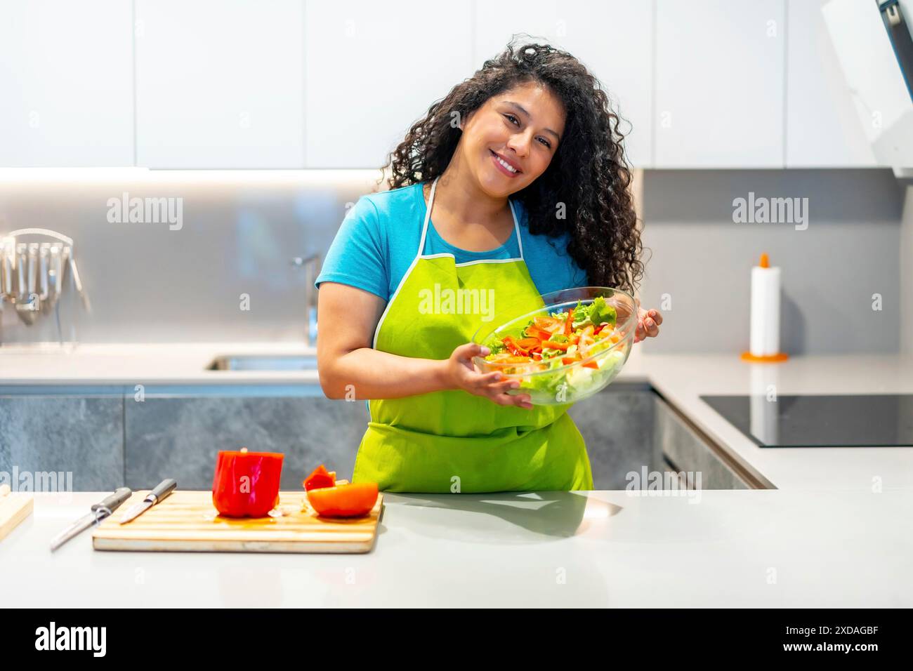 Latino giovane donna sorridente vlogger che mostra un'insalata sana alla macchina fotografica da casa Foto Stock